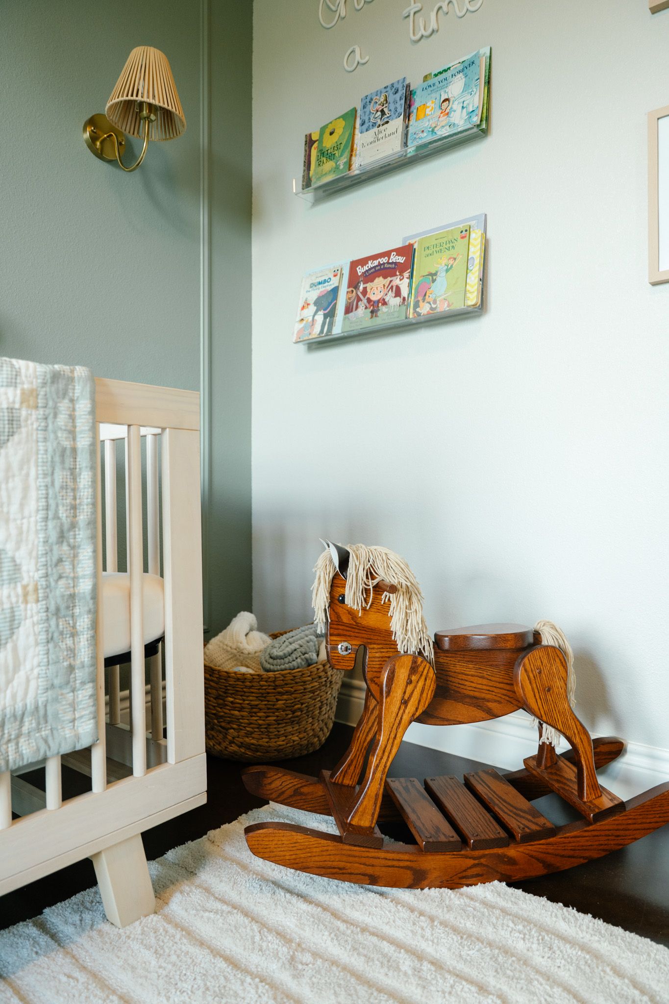 Cozy nursery corner with wooden rocking horse, white crib, and colorful children's books on wall shelves.
