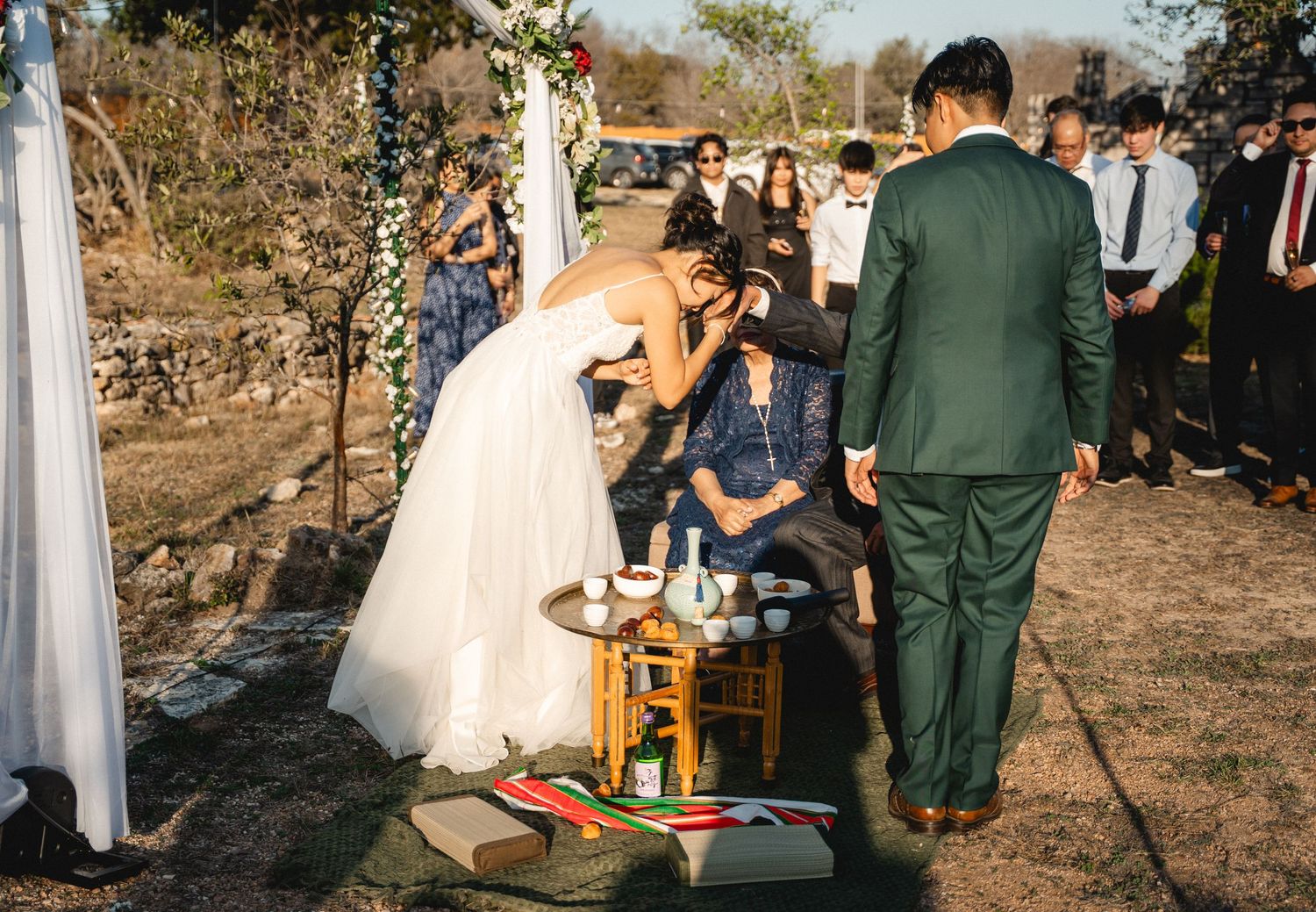 Bride bows respectfully during traditional Korean wedding tea ceremony at outdoor venue.