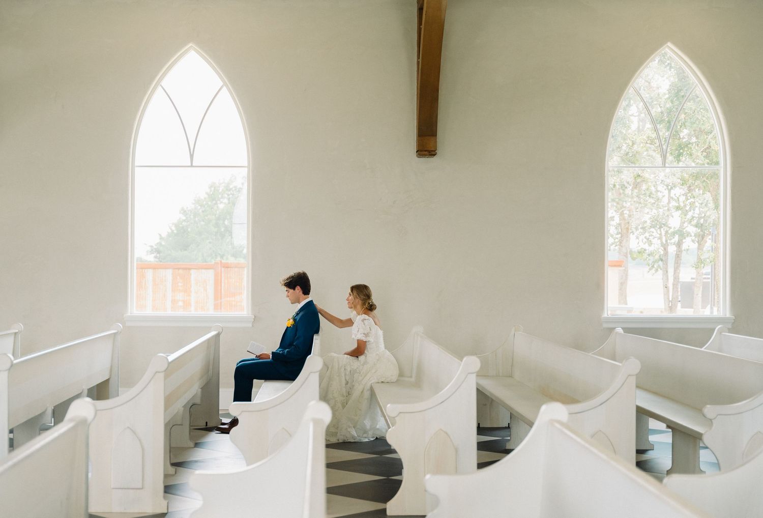 Bride and groom sharing an intimate moment seated in a white chapel with arched windows.