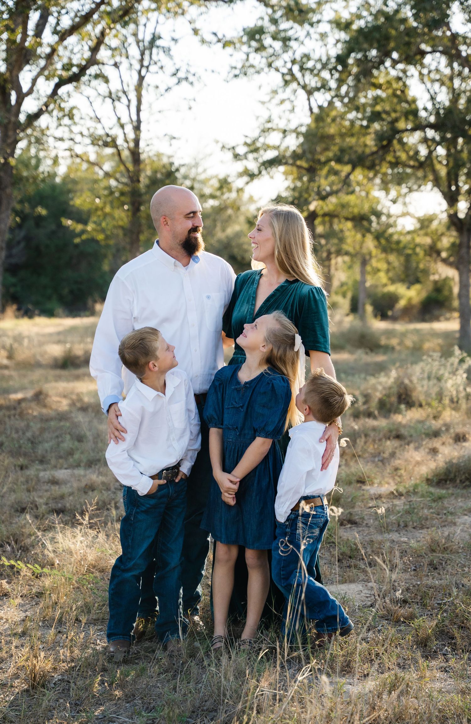 A happy family of five poses together in a golden sunlit outdoor field.