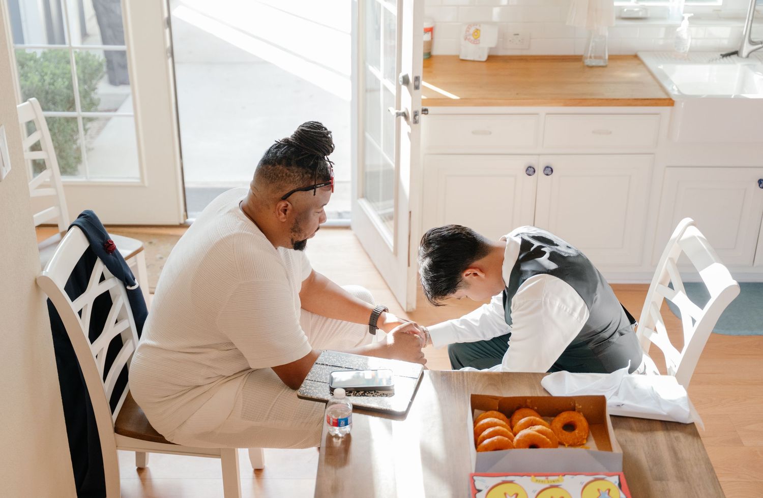 Groom and child writing together at kitchen table with donuts nearby.