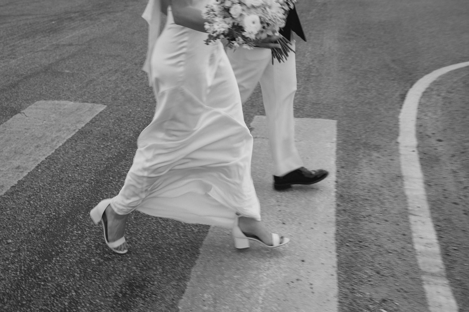Black and white photo of bride and groom crossing street in wedding attire.