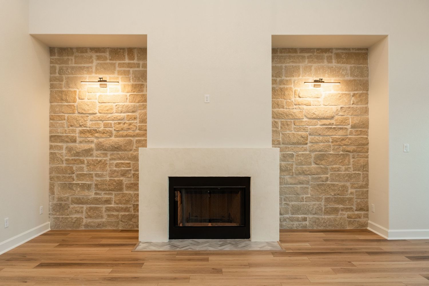 A modern living room fireplace flanked by stone accent walls with warm sconce lighting and hardwood floors.