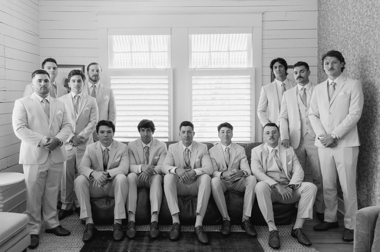 Black and white portrait of groom and groomsmen in light suits posing together in a bright room.