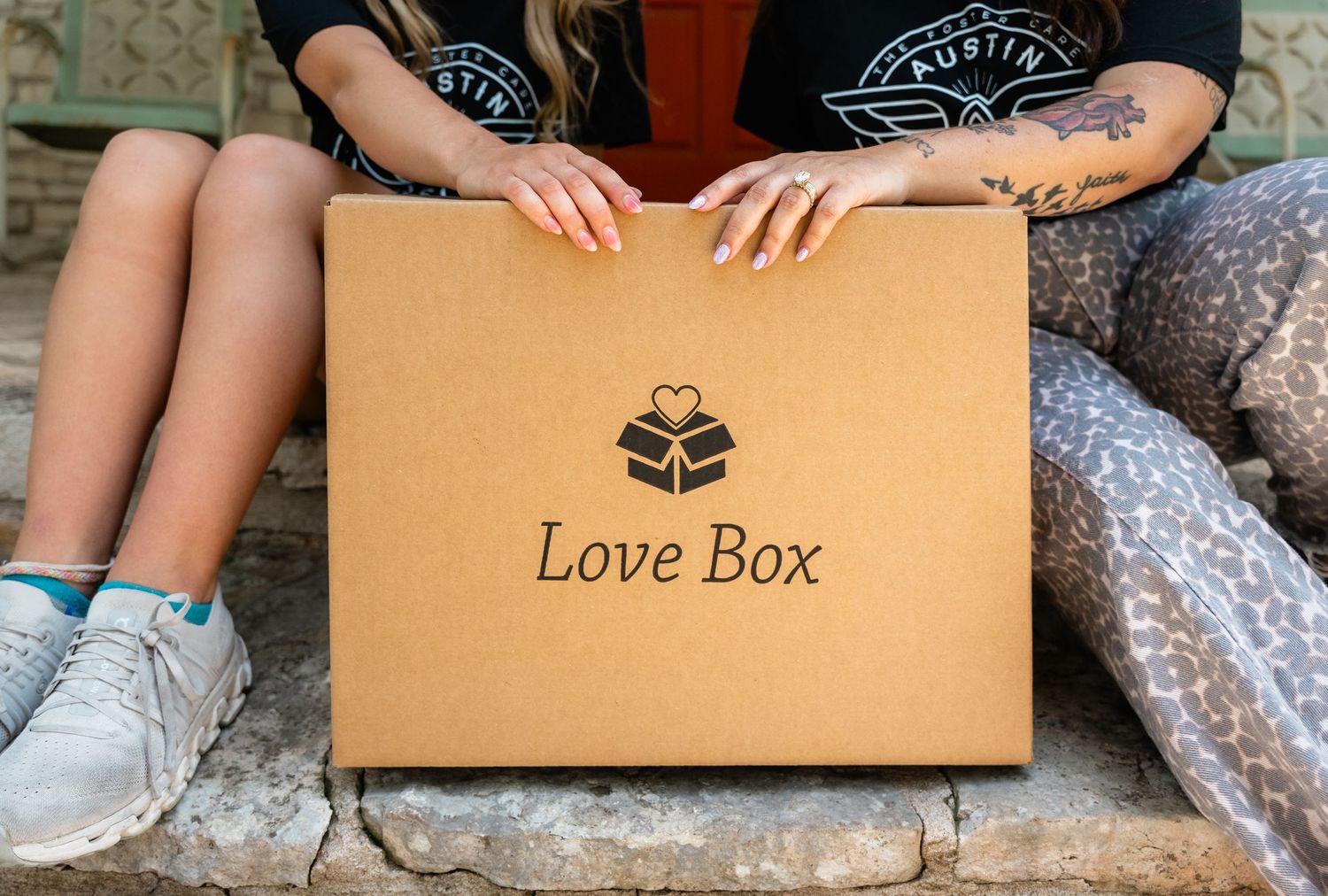 Person holding a kraft cardboard Love Box with heart logo while sitting on stone steps.