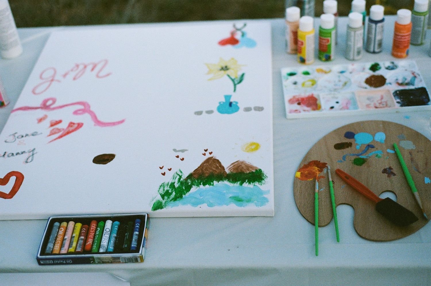 Colorful wedding guest book painting station with paints, brushes, and canvas artwork.