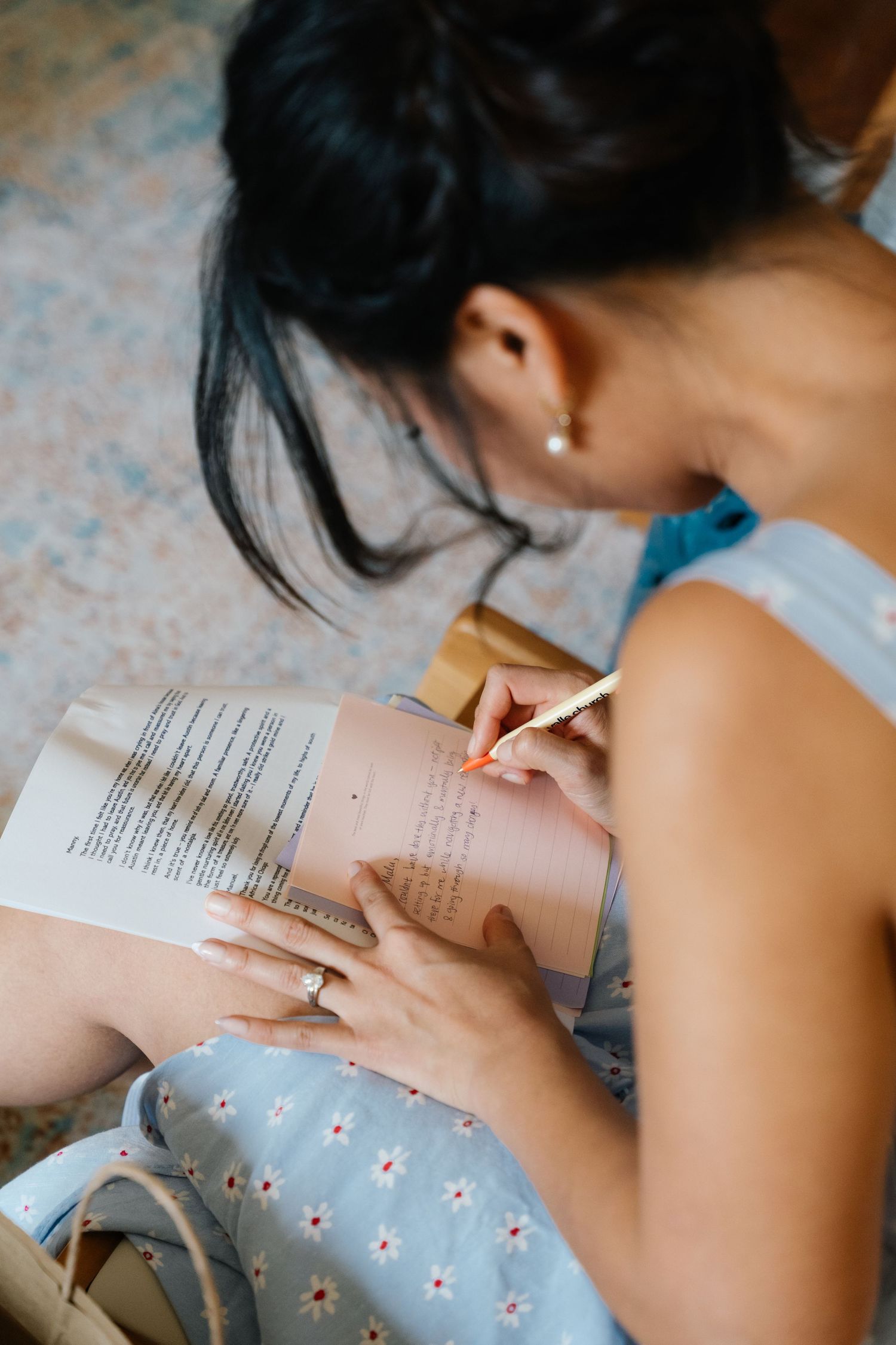 Bride in floral dress annotating wedding vows in a book with a pencil.