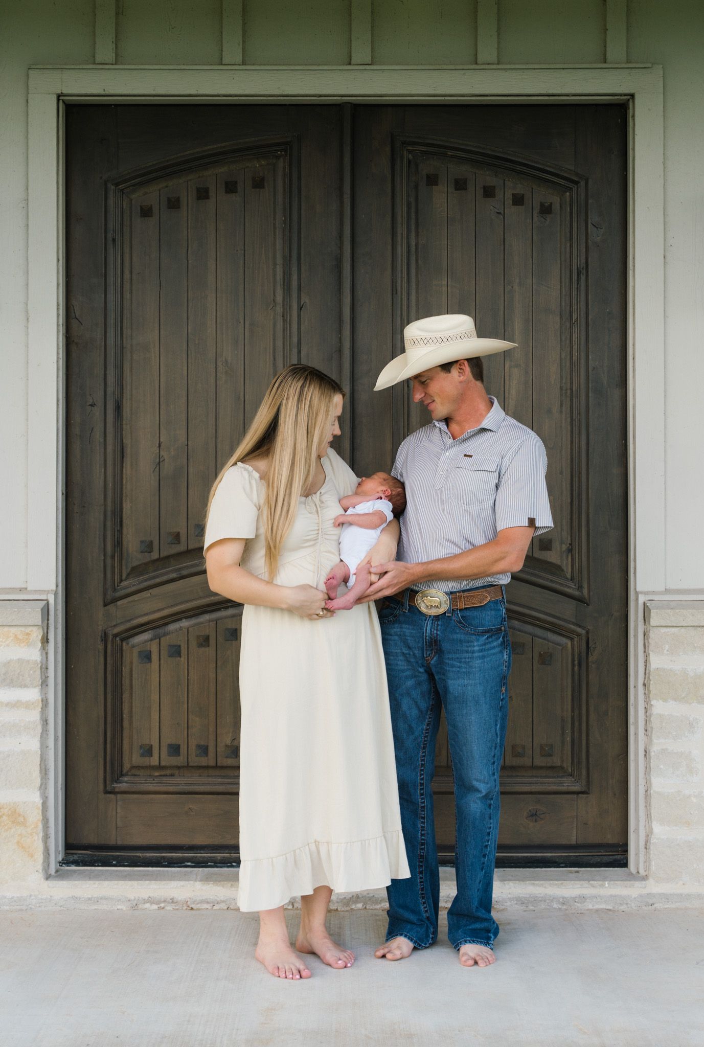 New parents holding their son on their front porch during newborn session in East Bernard, Texas.