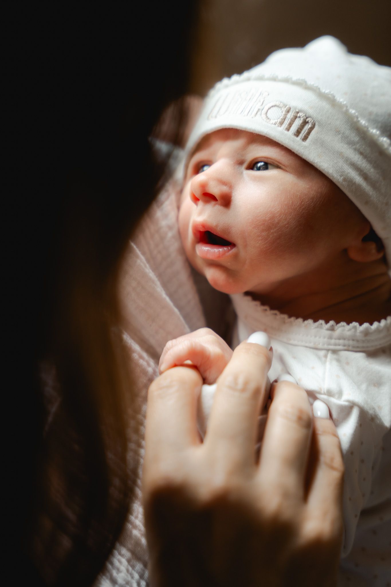 Close-up of newborn baby in white hat being cradled by mothers hands.