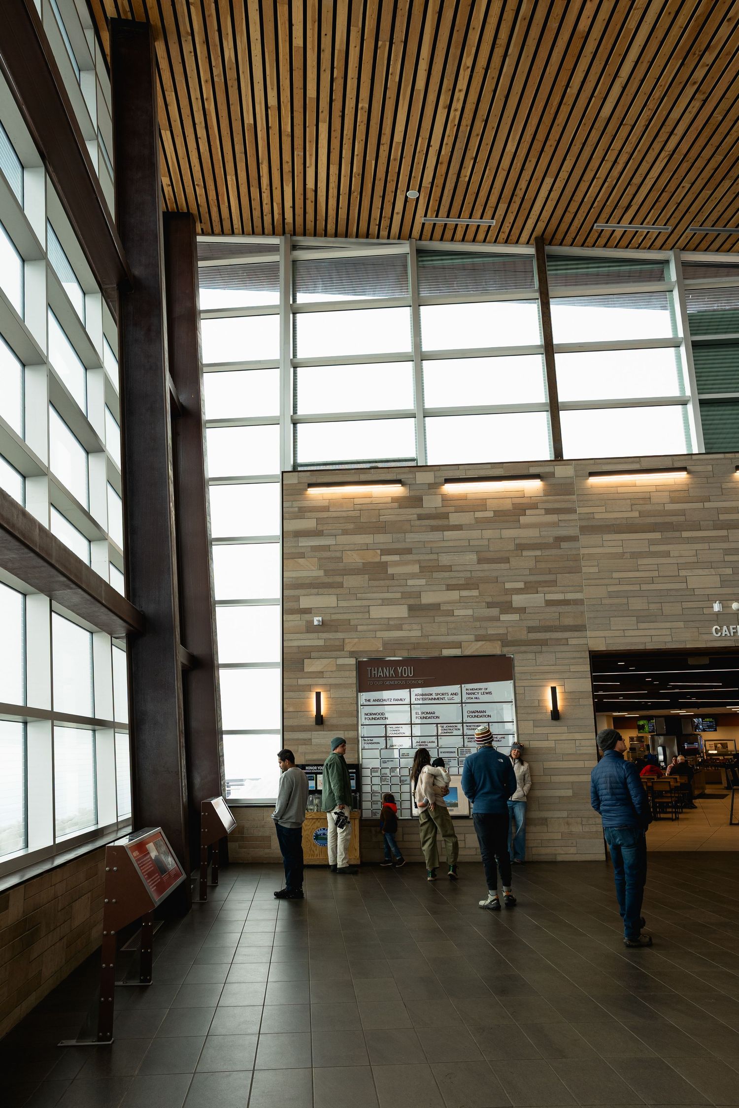 Visitors browse an information display in a modern visitor center with large windows and wood-paneled ceiling.