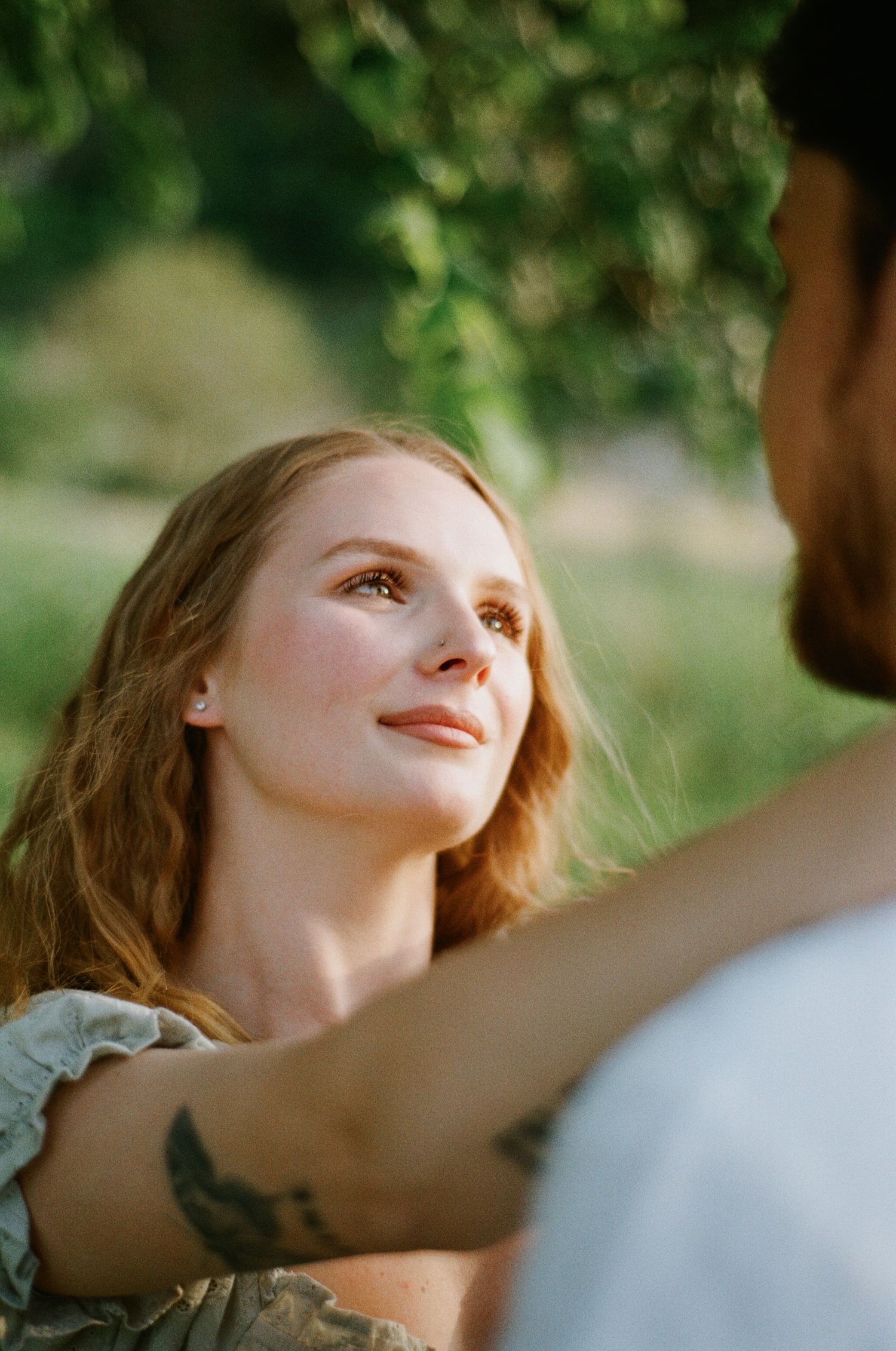Smiling redhead woman with freckles gazes up lovingly at her partner outdoors in golden sunlight.