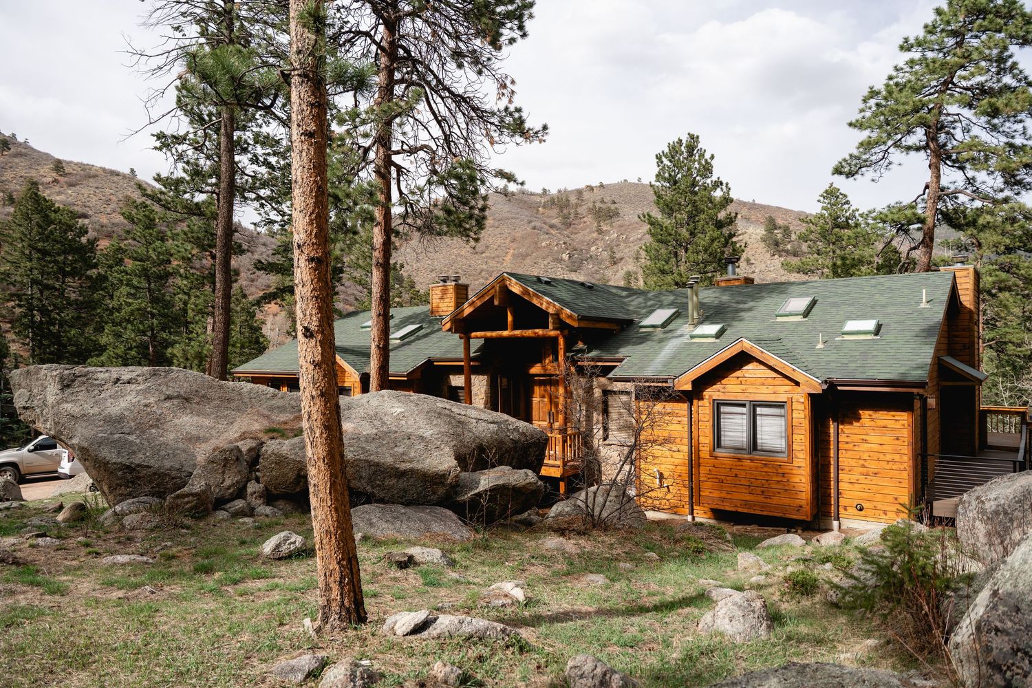 Rustic log cabins nestled among pine trees and large boulders in a scenic Colorado mountain landscape.