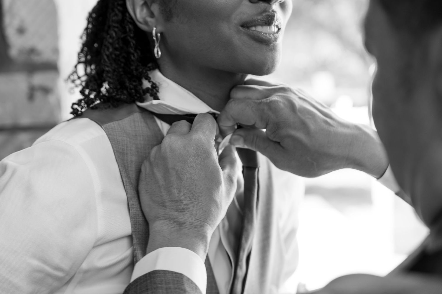 Close-up black and white photo of someone adjusting a tie before wedding.