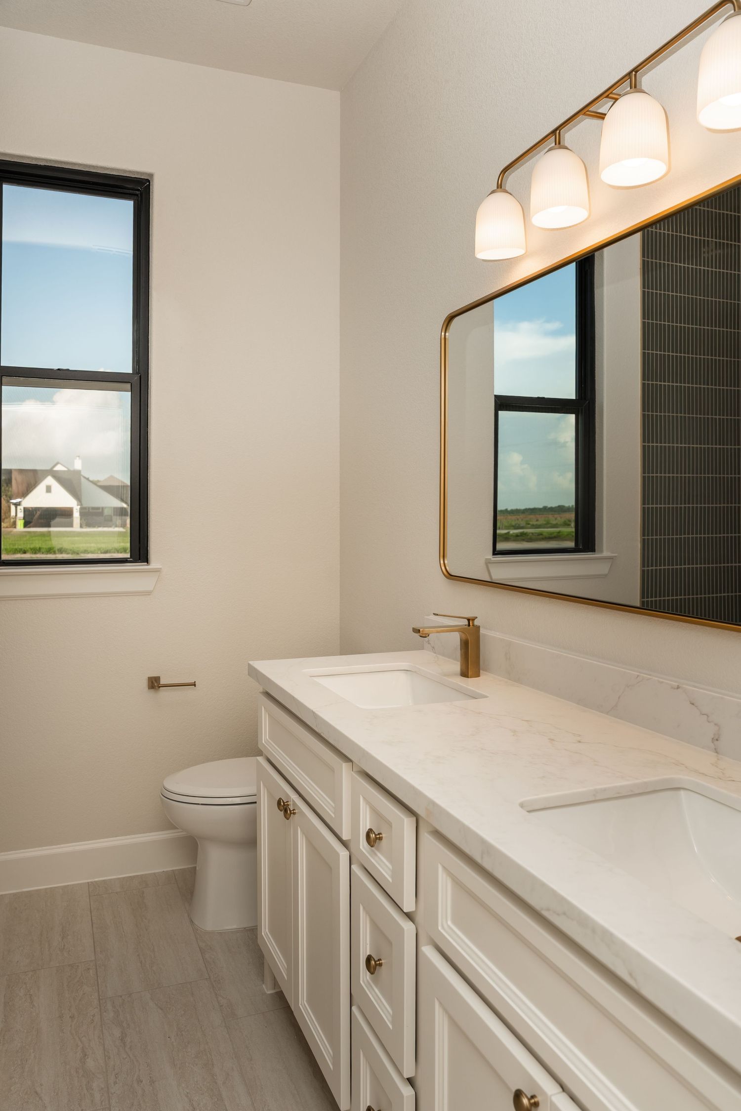 Classic white bathroom vanity with marble countertop, gold fixtures, black-framed mirror, and subway tile accents.