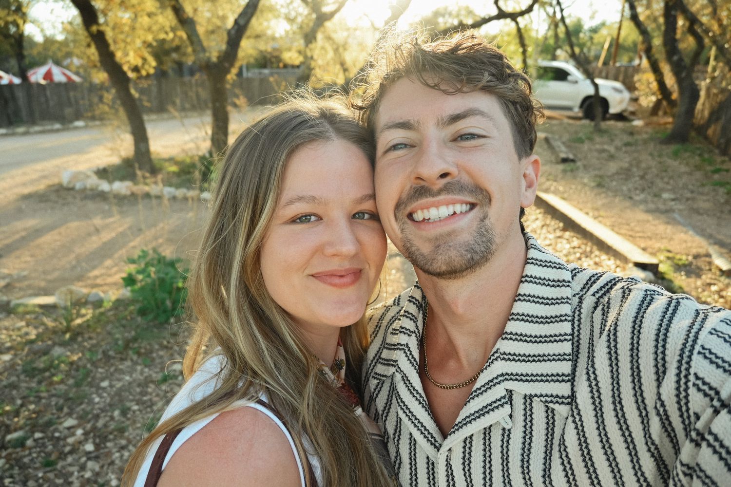 Smiling couple taking a sunny outdoor selfie at a rustic Texas glamping resort.