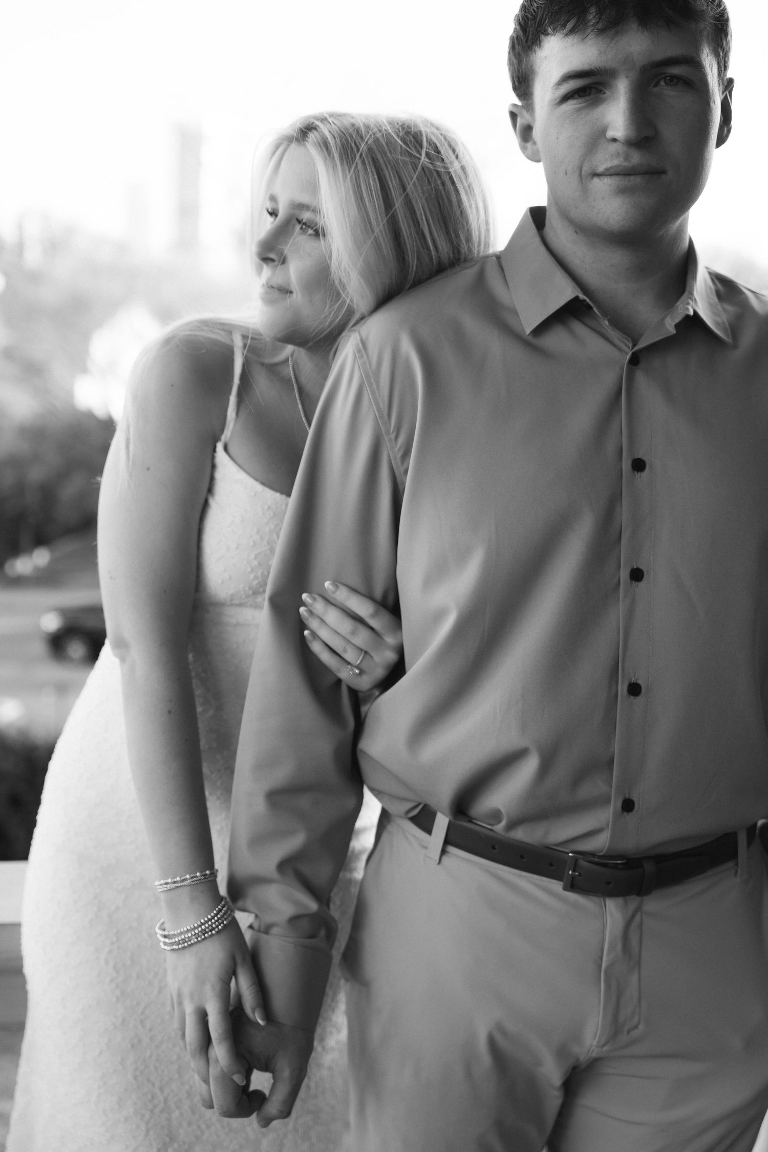 Black and white portrait of couple, woman in spaghetti strap dress leaning on mans shoulder tenderly.
