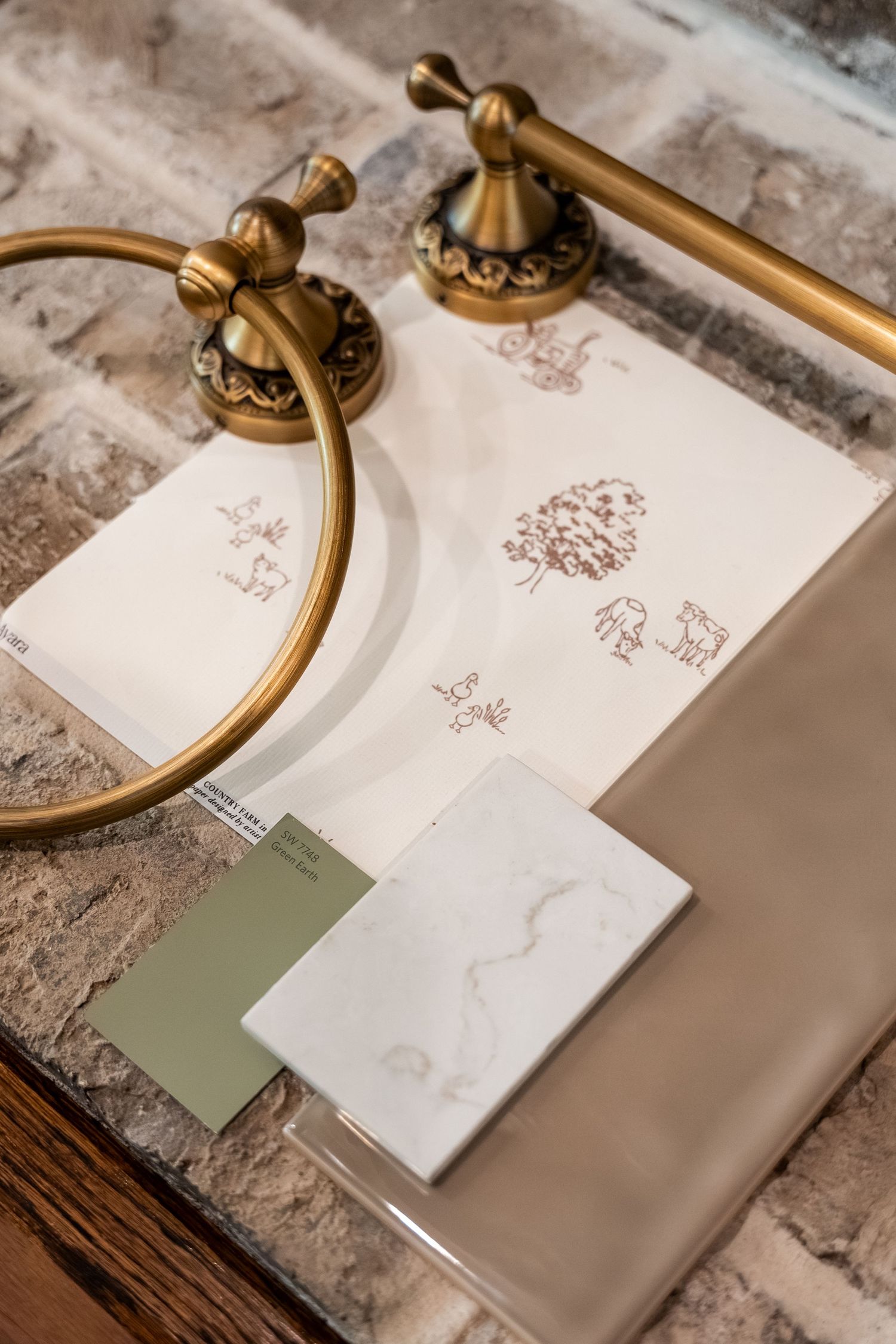 Brass bathroom hardware and fixtures displayed with paint swatches and stone samples on brick surface.