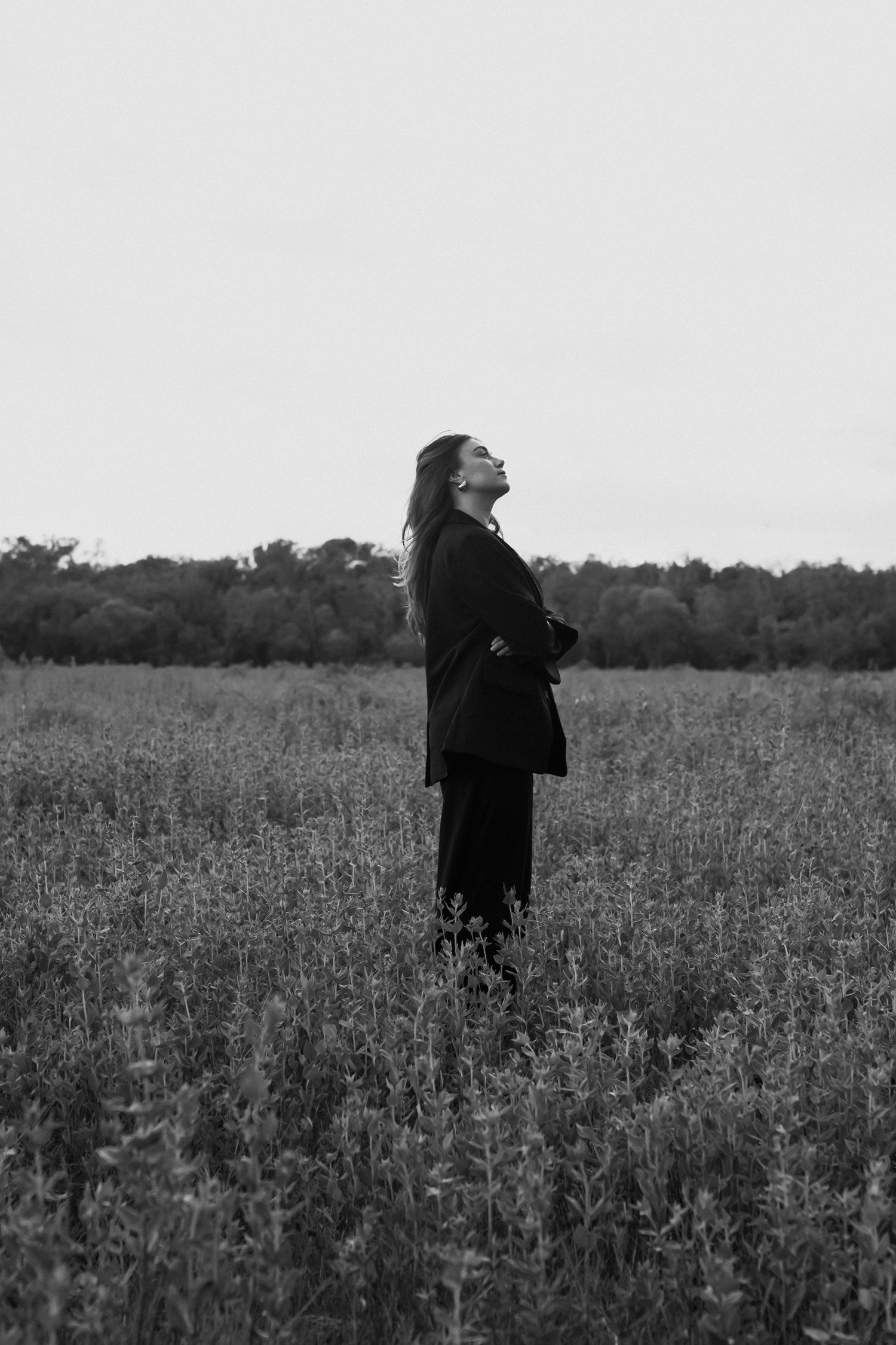 Black and white photo of a woman standing in a field with head tilted back, wearing a dark blazer.