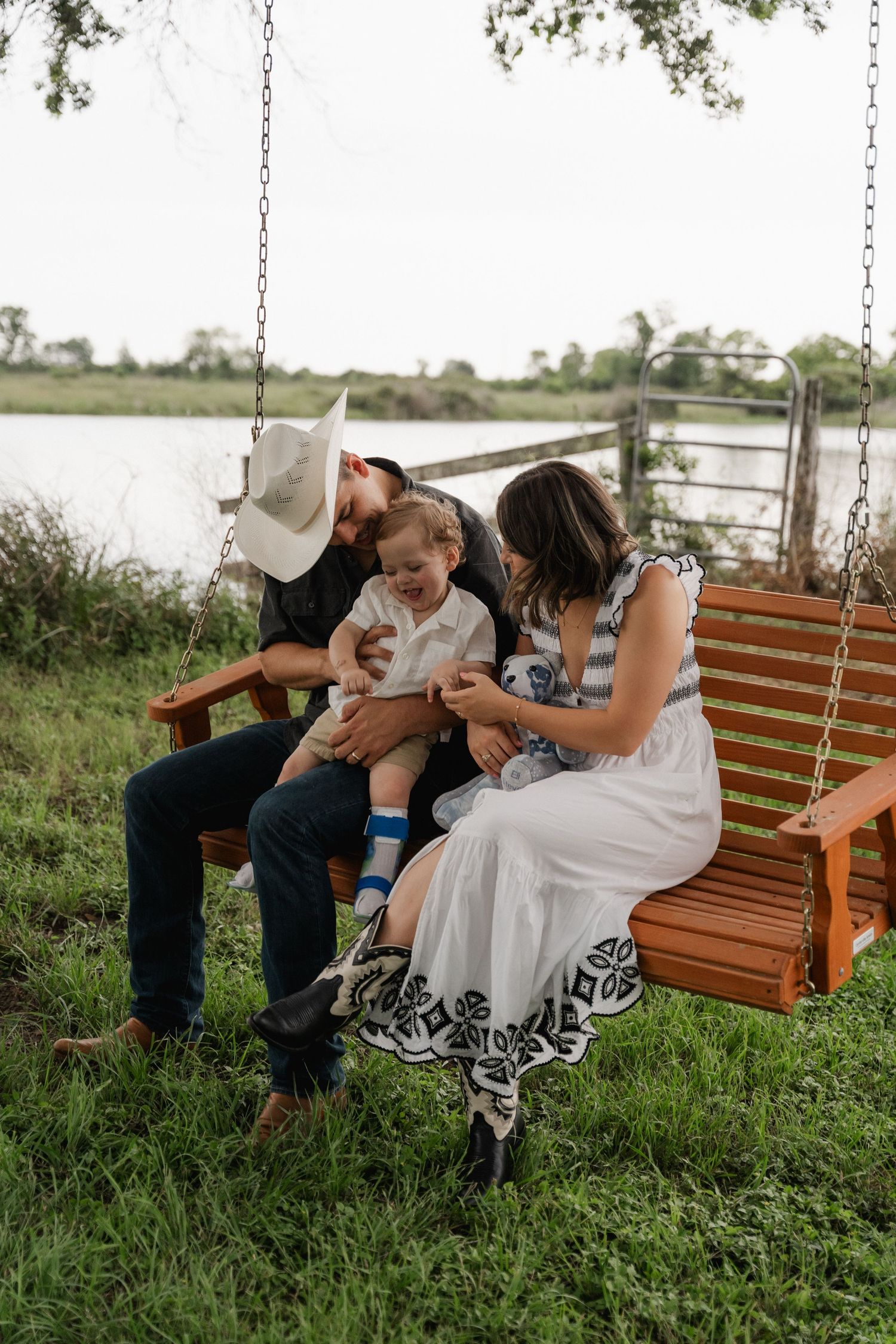 Happy family with young child sitting together on a wooden porch swing near a peaceful lake.