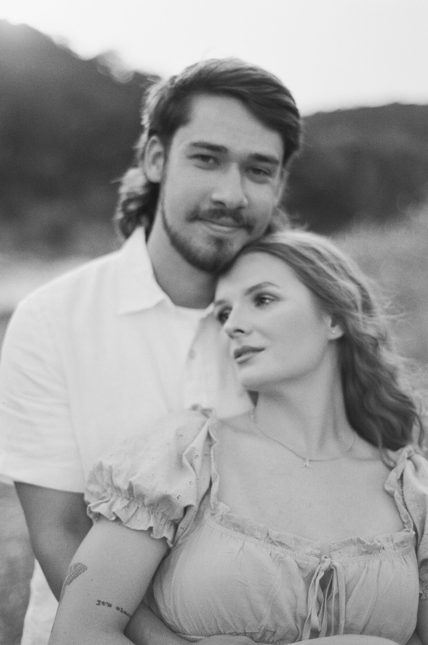 Black and white romantic couple portrait outdoors, woman leaning on mans shoulder, soft natural light.