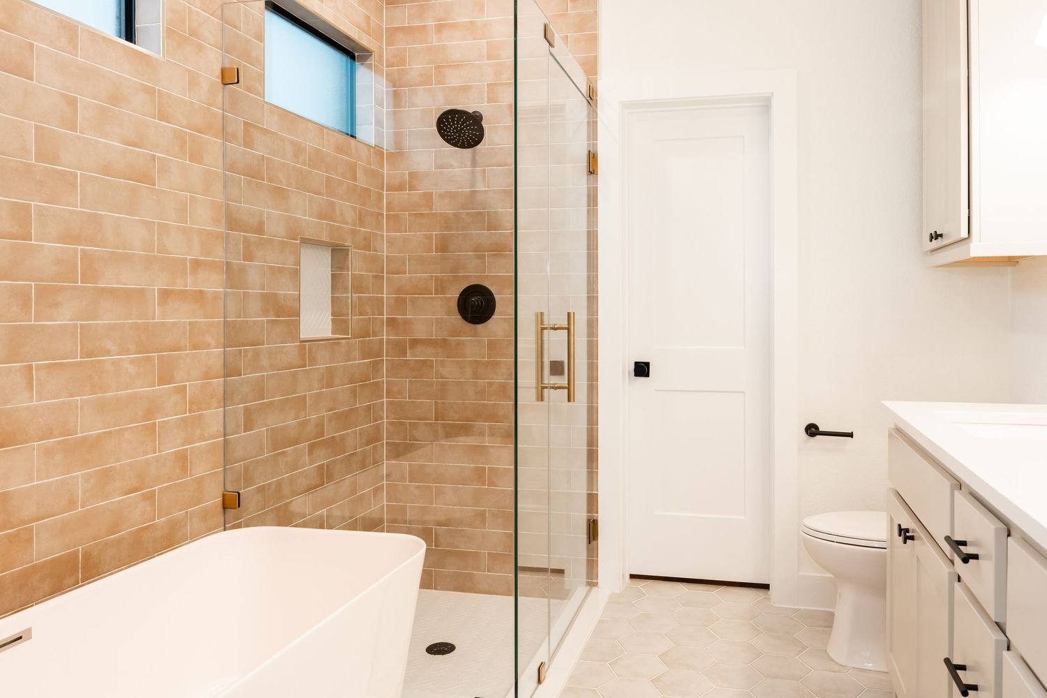 Modern bathroom with beige tile walk-in shower, freestanding tub, and glass door.