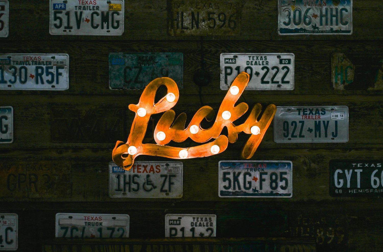Glowing Lucky marquee sign surrounded by vintage Texas license plates on a wooden wall.