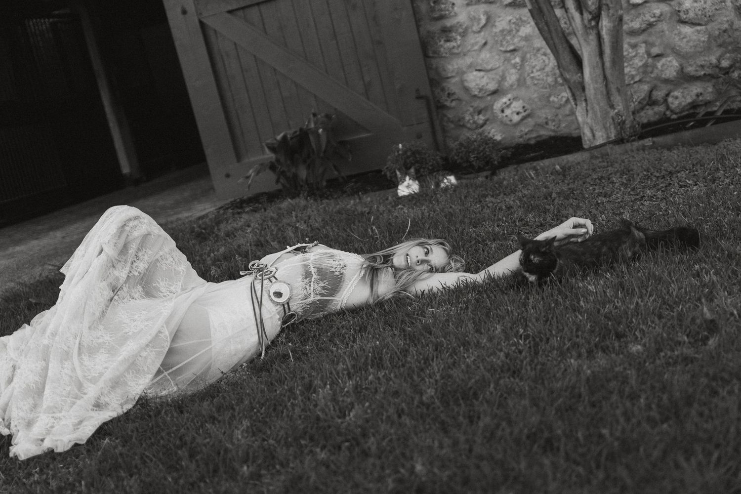 Woman in white lace dress lying on green grass in black and white outdoor photo.