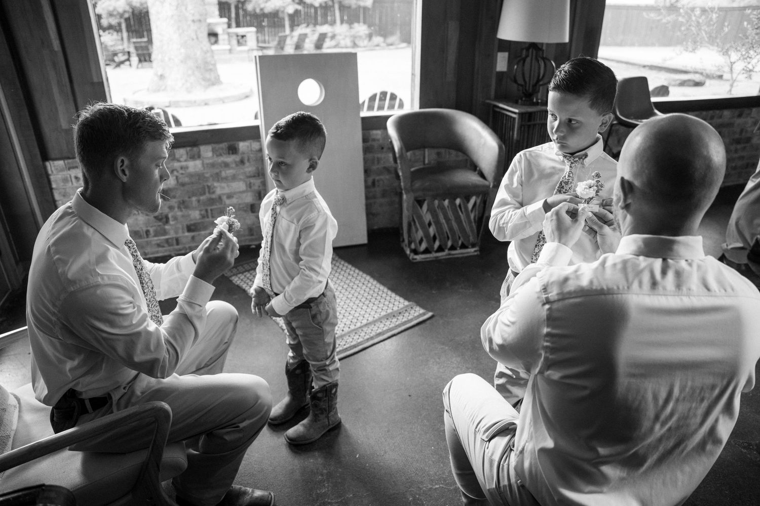 Black and white photo of groomsmen and a young boy in white shirts chatting in a rustic lounge.