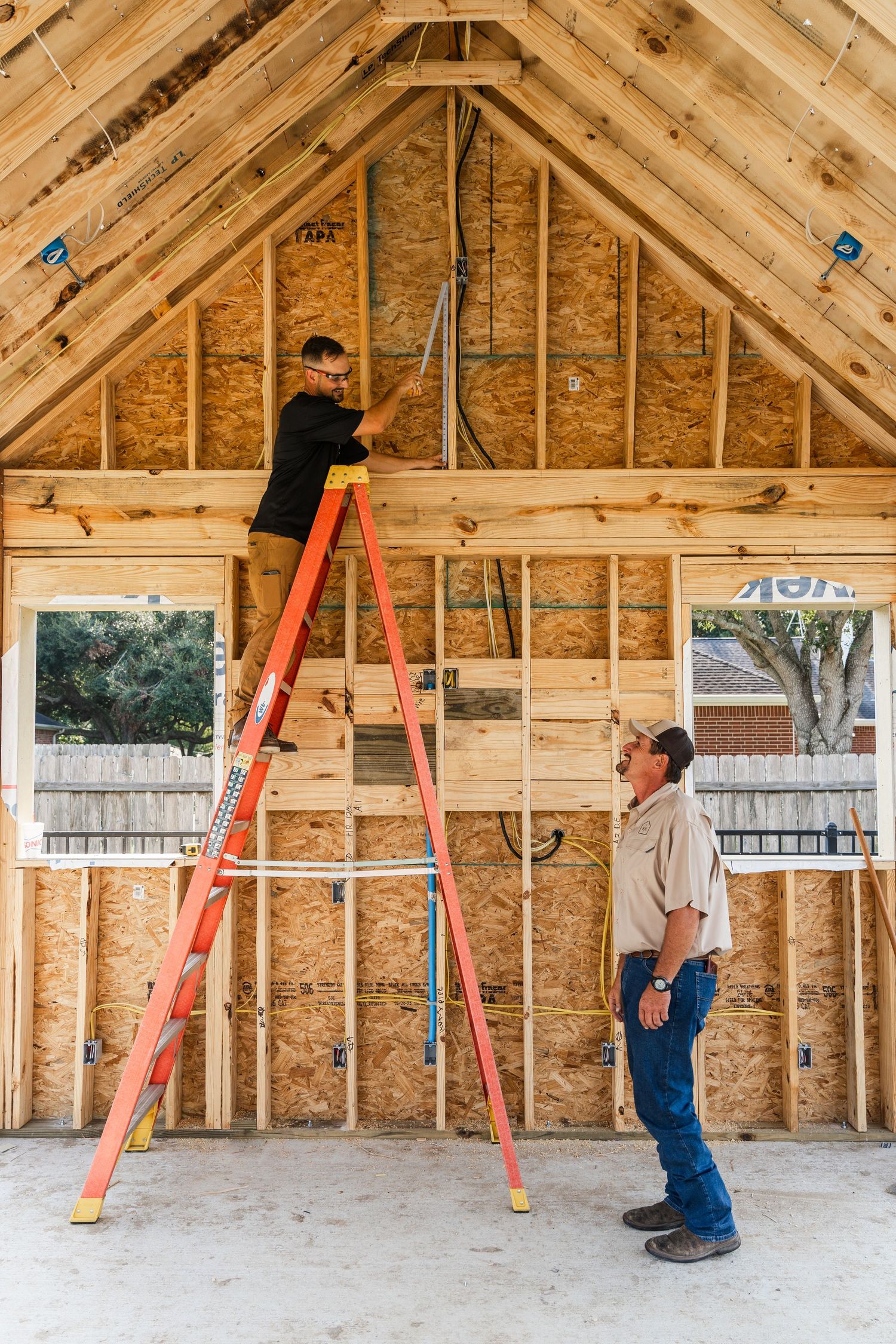 Two construction workers on an orange ladder framing the interior of a new home being built.