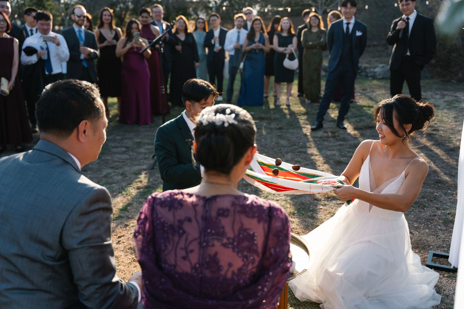 Bride presents gift during traditional Korean wedding ceremony with seated family elders.