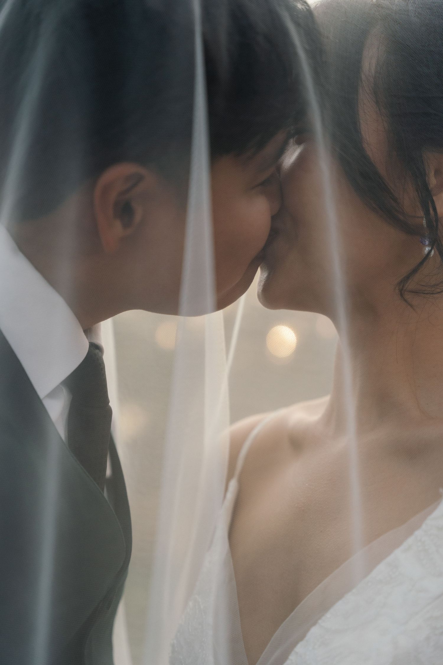 Intimate close-up of bride and groom nearly kissing beneath a flowing white wedding veil.