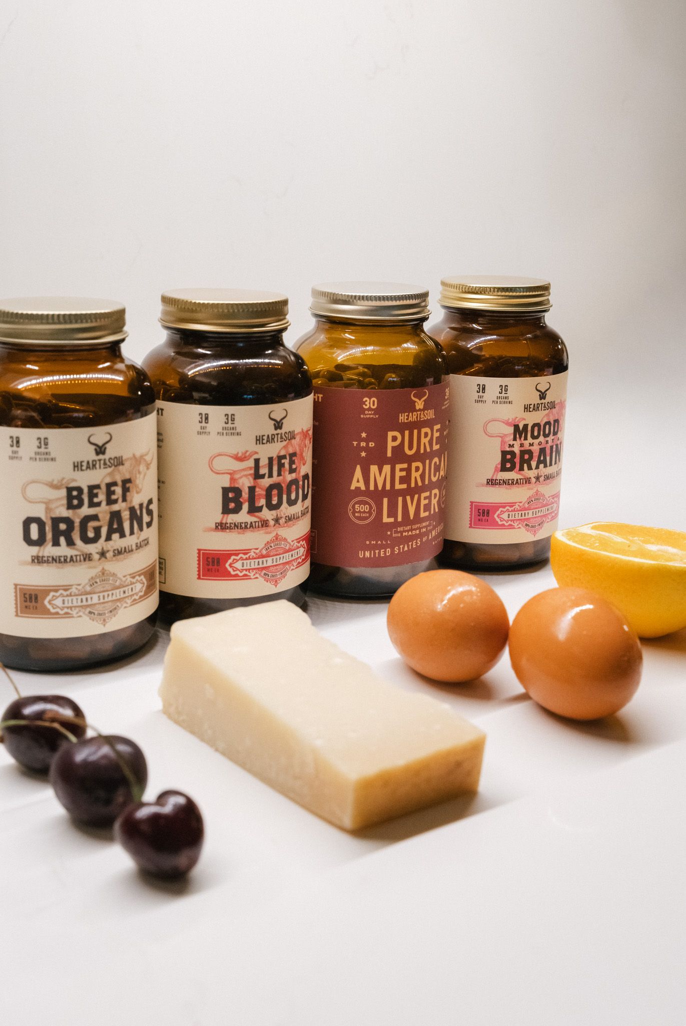 Four Hearticon supplement jars including Beef Organs and Life Blood, displayed with eggs, cherries, cheese, and lemon.