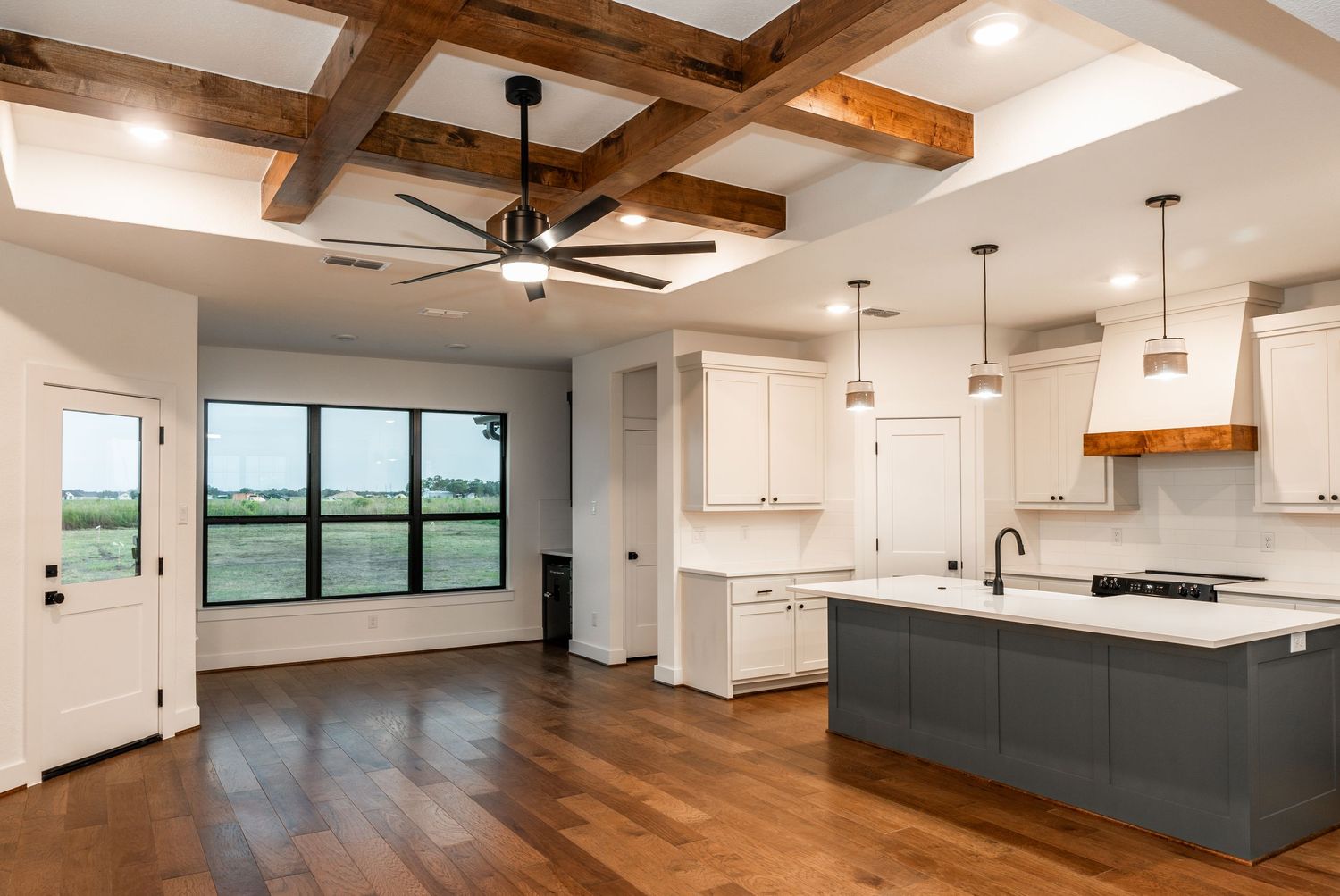 Modern farmhouse kitchen with white cabinets, gray island, hardwood floors, and rustic wood beam coffered ceiling.