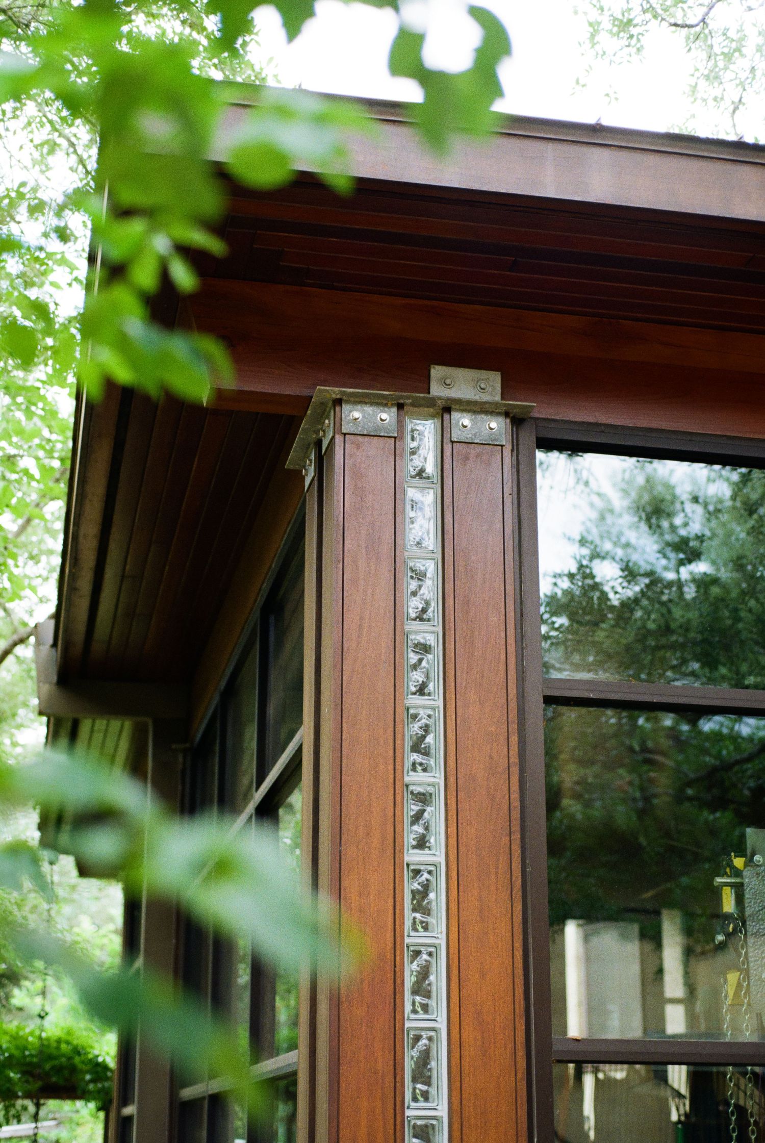 Close-up of ornate wooden architectural column with decorative metal inlay details on a Prairie-style glass and wood structure.