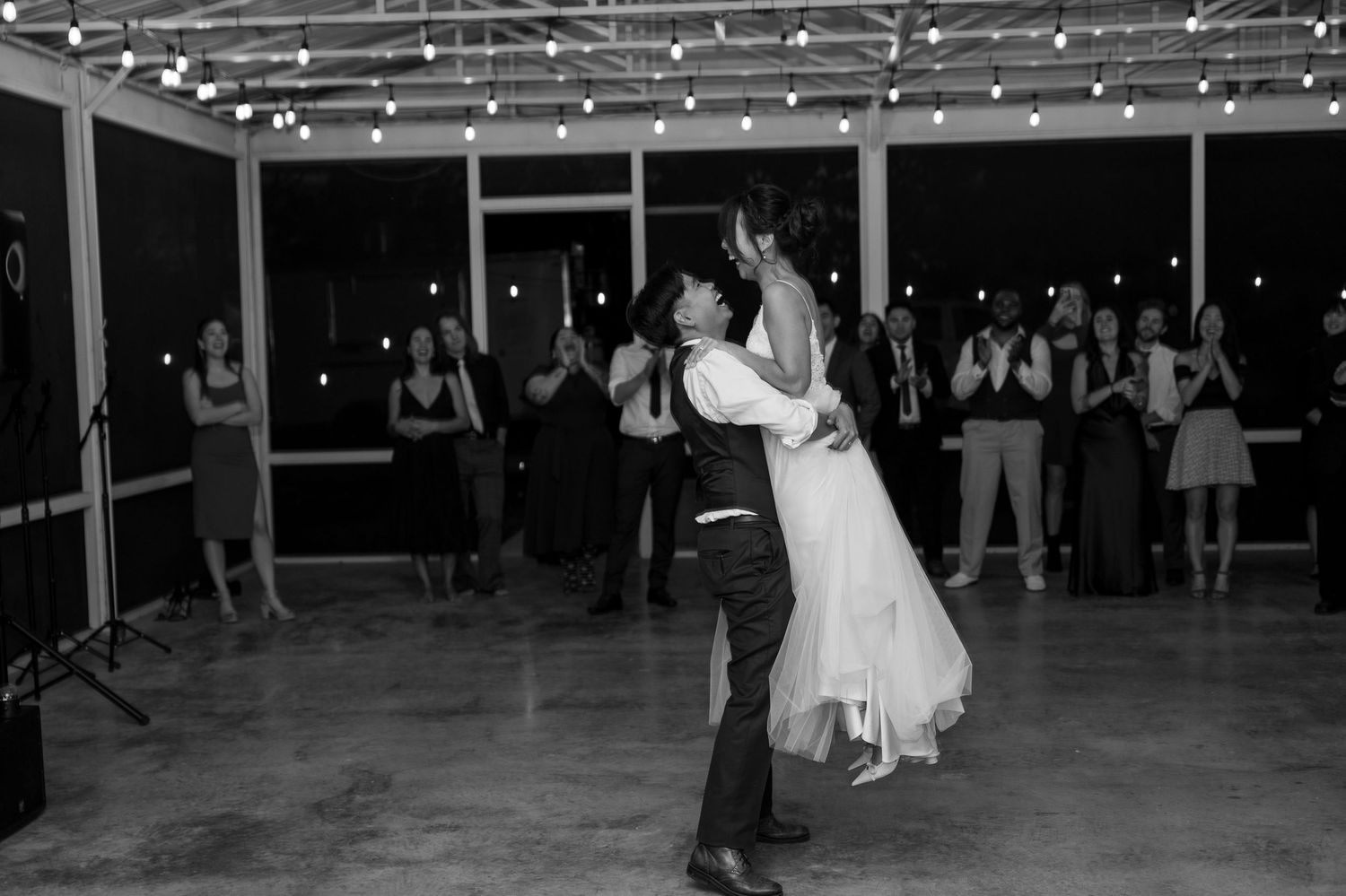 Black and white photo of groom lifting bride during romantic first dance at wedding reception.