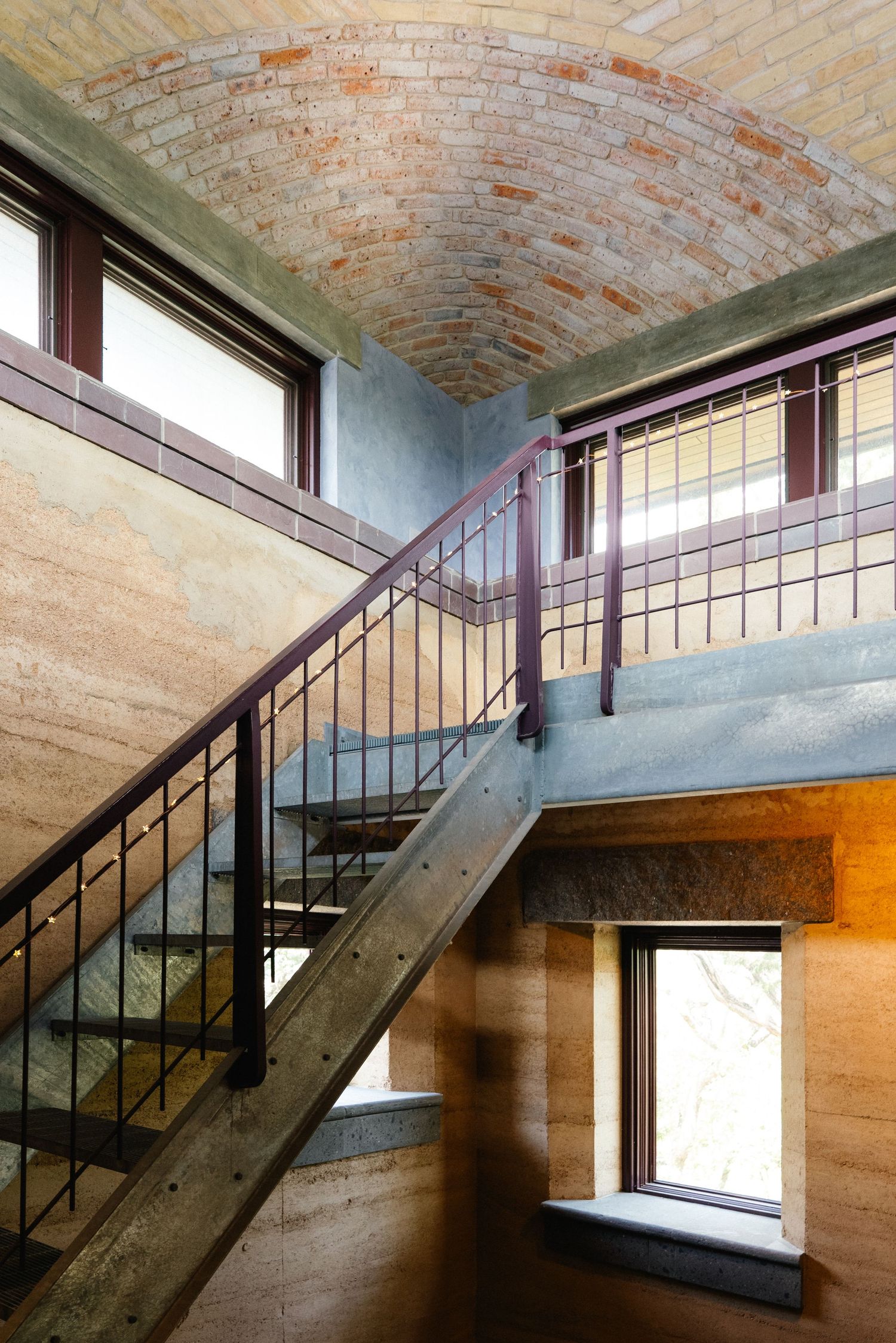 Industrial-style interior staircase with metal railings beneath a barrel-vaulted brick ceiling with natural light from windows.