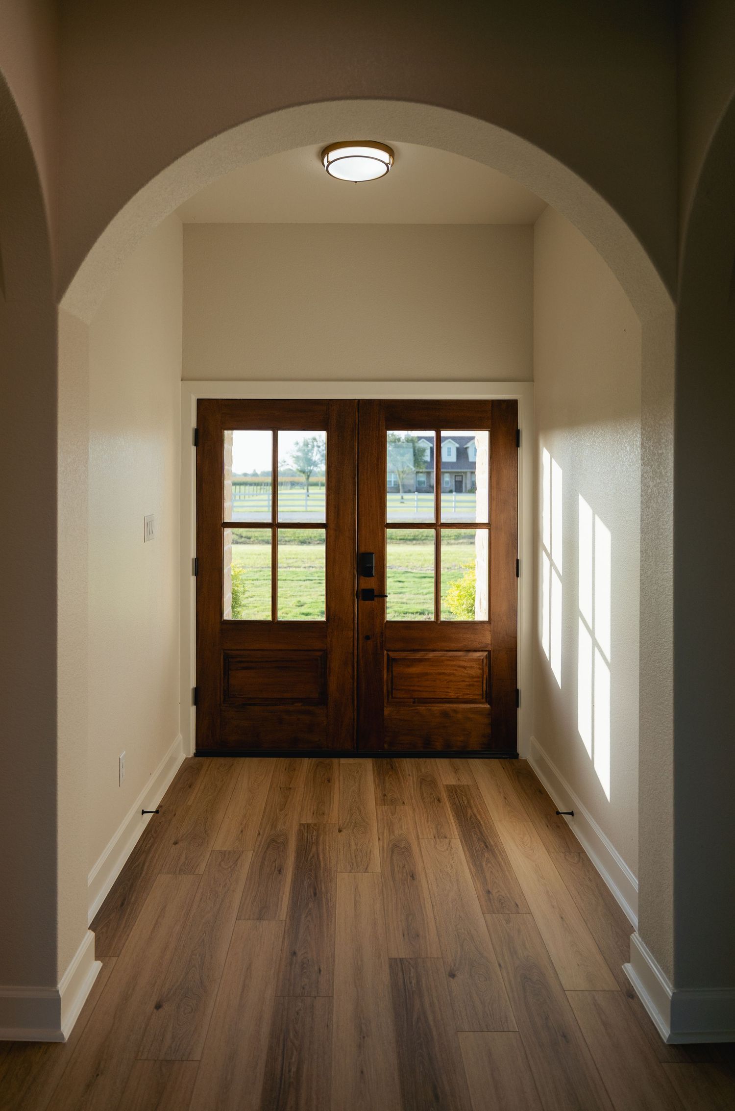Elegant home entryway with arched doorway, hardwood floors, and wooden double doors with glass panels.