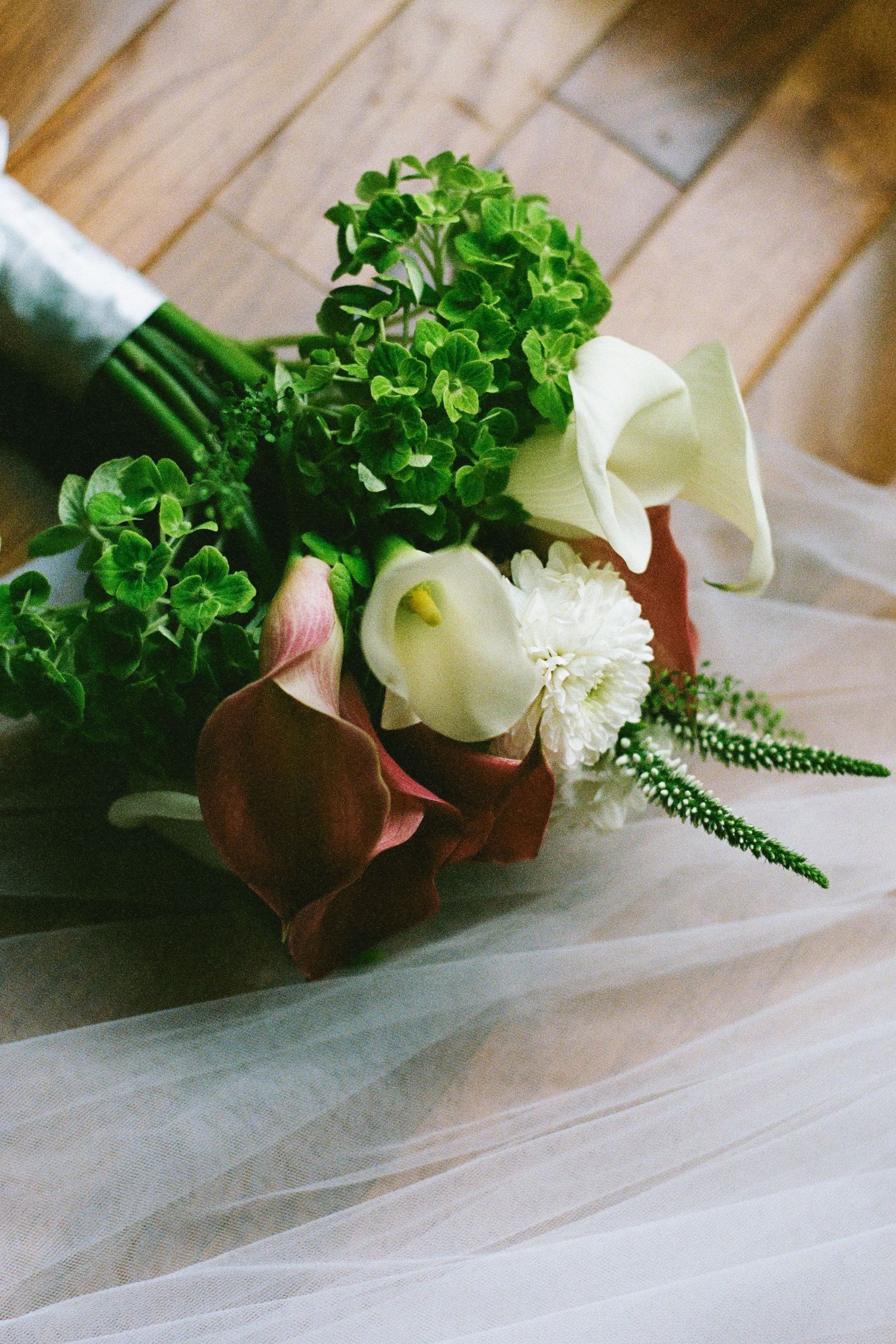 Wedding bouquet with white calla lilies, green hydrangeas, and red flowers on veil.