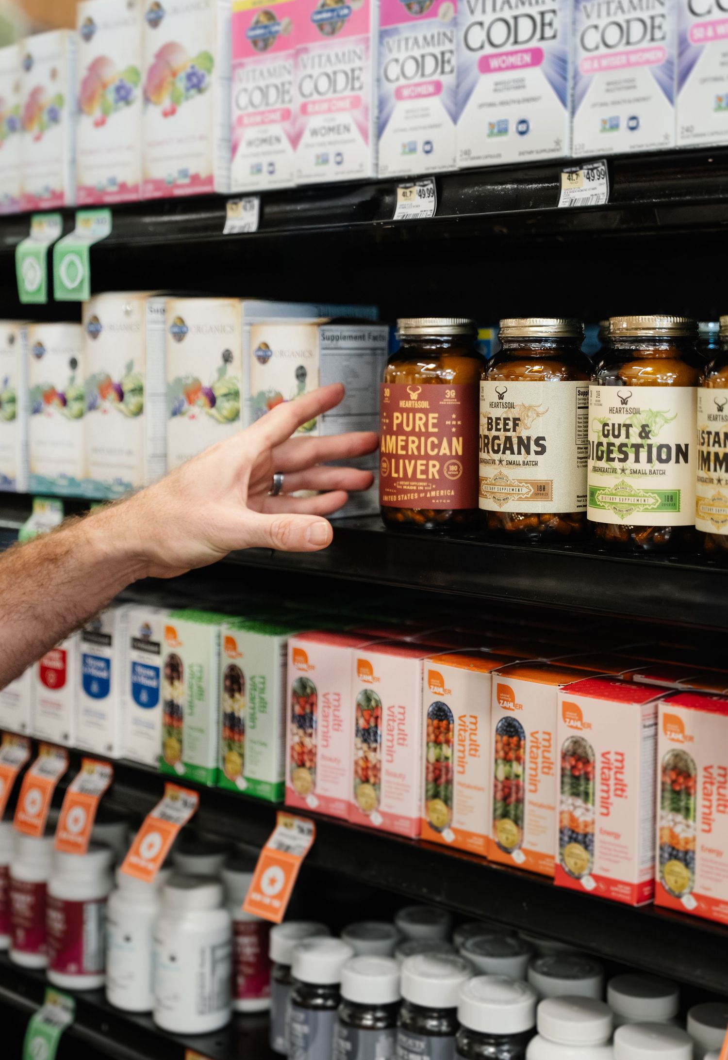 Hand reaching for Pure American Liver supplement jar on health store shelf with vitamins and supplements.