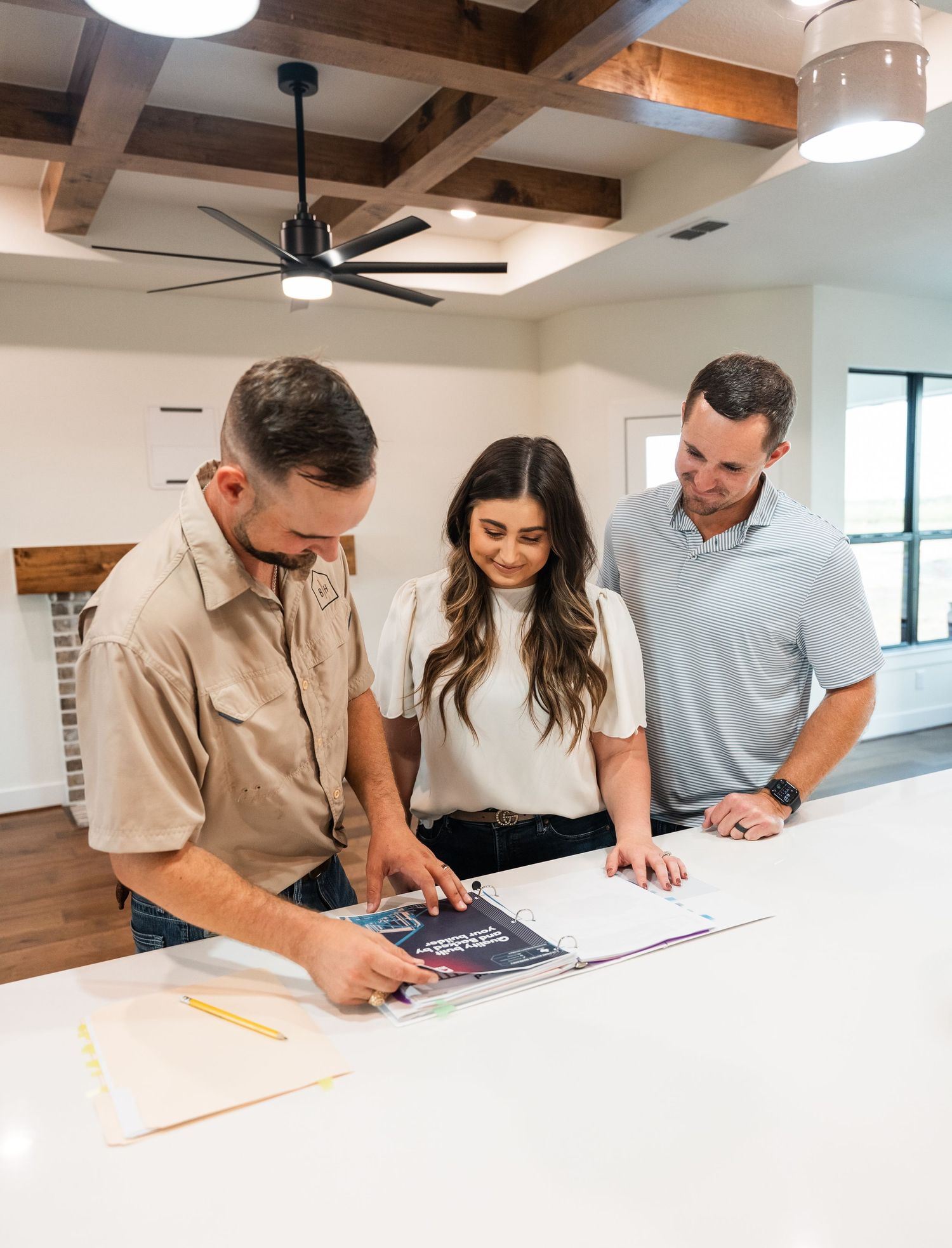 Three professionals review construction plans on a white countertop in a modern home.