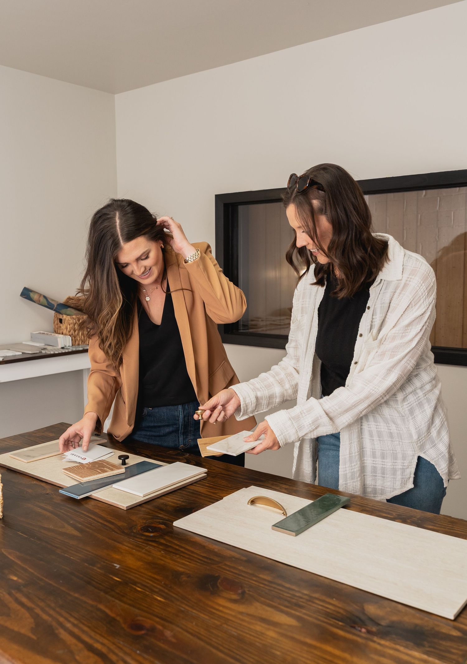 Two women reviewing material samples and swatches on a wooden table in a modern interior design studio.