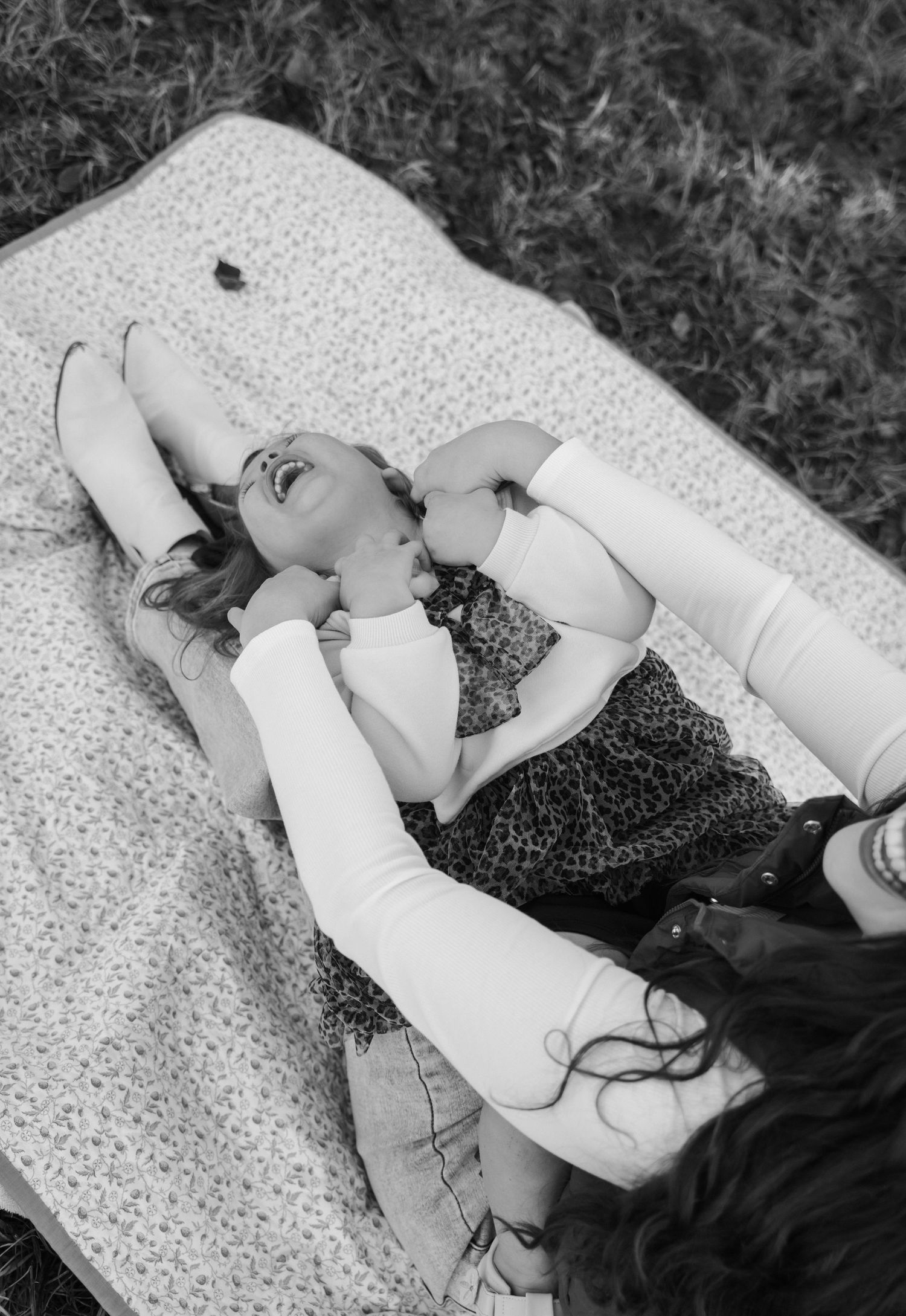 Black and white aerial view of a mother and daughter laughing together on a blanket in the grass.