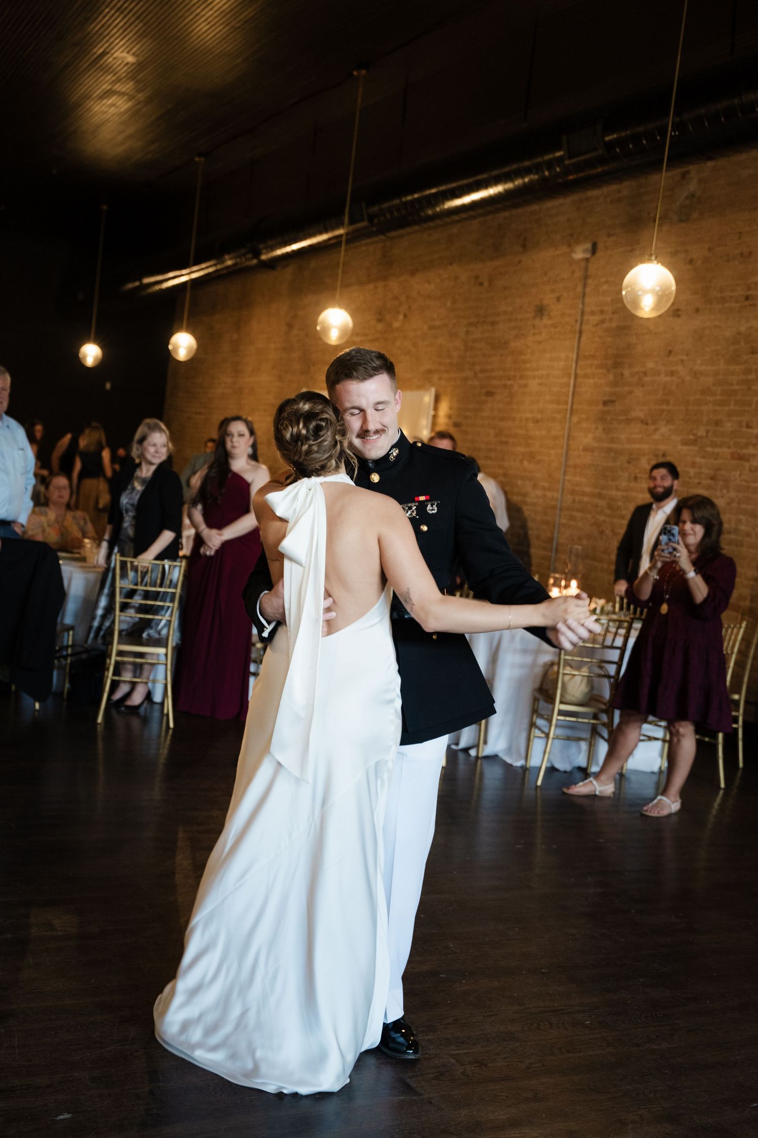 Military groom and bride sharing first dance in warmly lit reception venue.