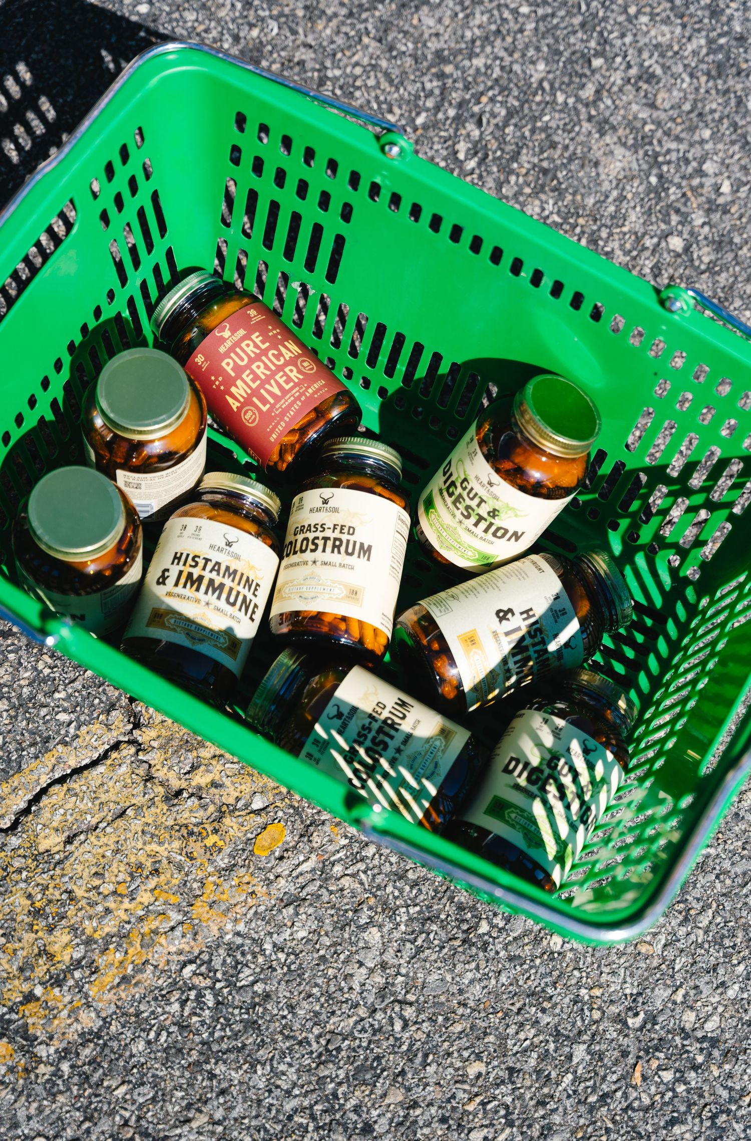 Green basket filled with amber glass supplement jars including Histamine & Immune and Grass-Fed Colostrum bottles.