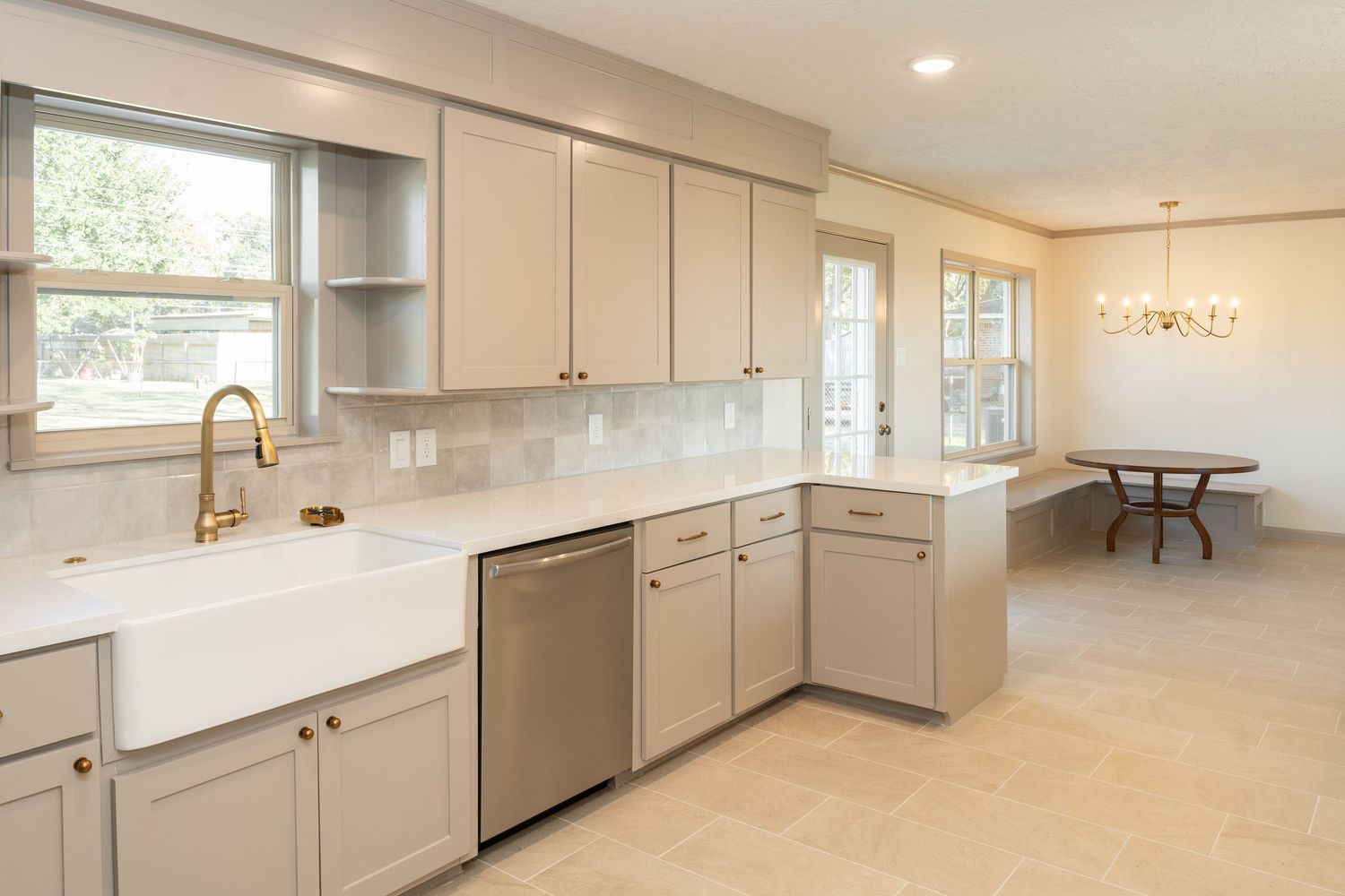Bright kitchen remodel with gray cabinets, white quartz counters, farmhouse sink, gold faucet, and subway tile backsplash.