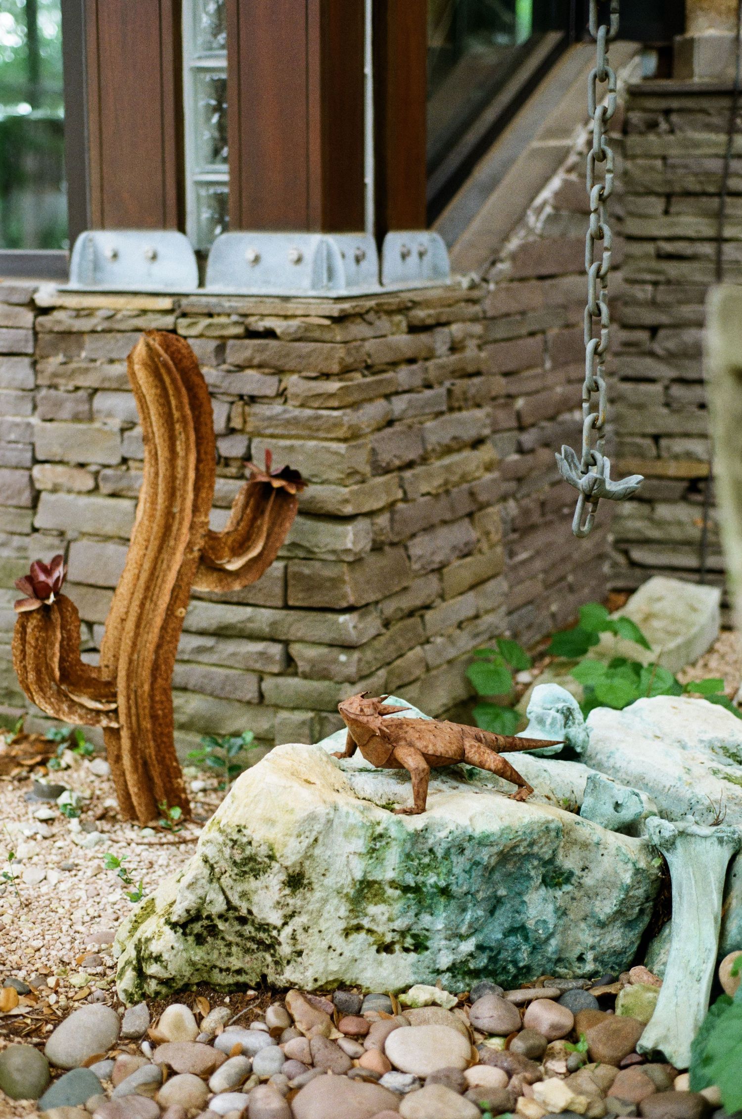 Rustic garden with metal cactus sculpture, lizard figurine, and stone wall decor.