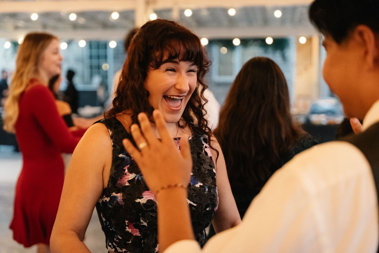 Woman in floral dress laughs joyfully while conversing with guest at elegant wedding reception.