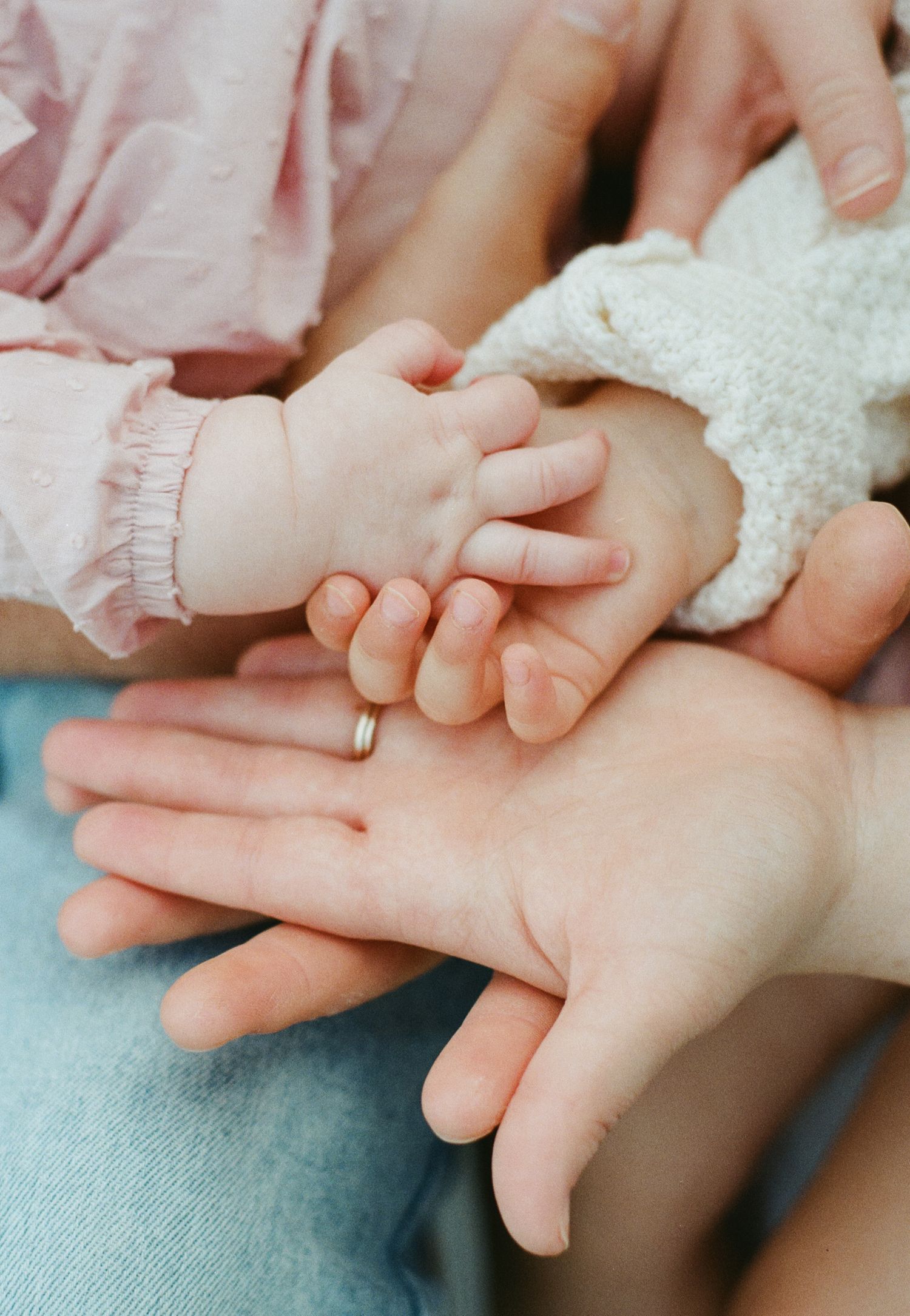 A close-up of a newborn baby's tiny hand resting on parents' and sibling's hands together.