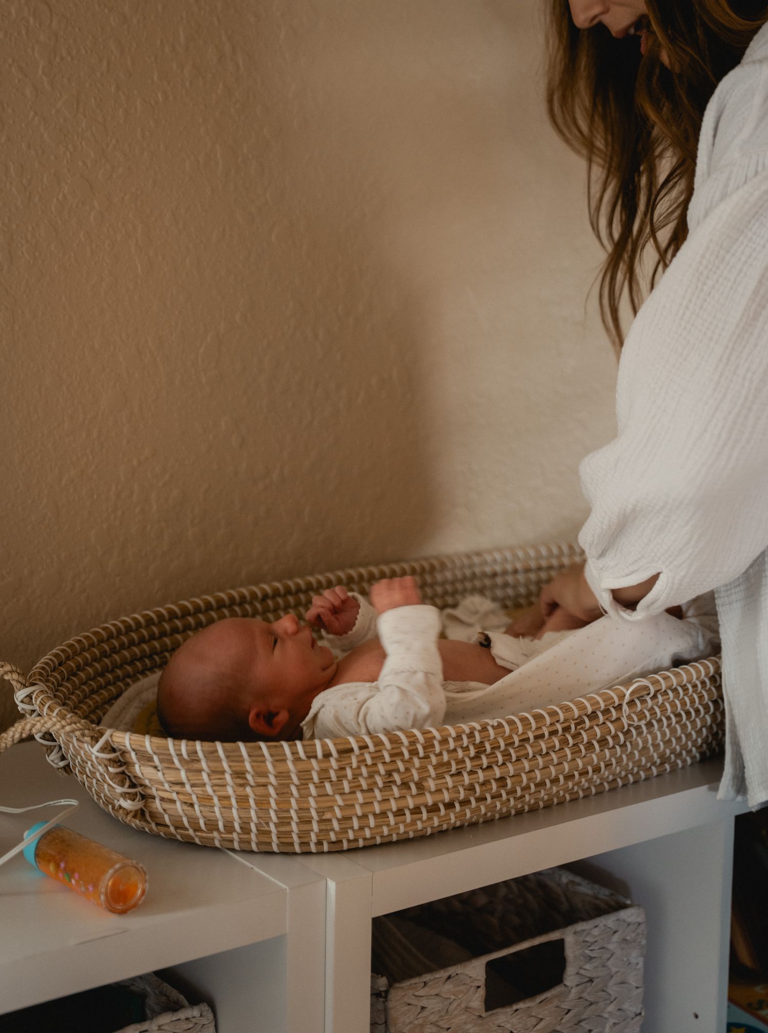 Mother in white robe tenderly cares for newborn baby lying in a wicker basket.
