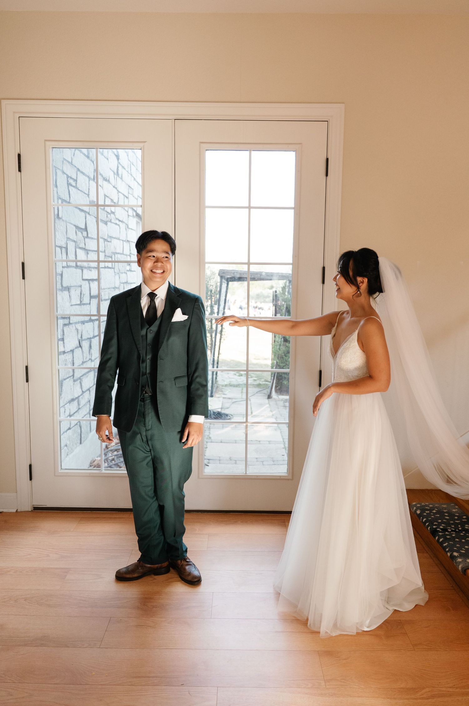 Groom smiling joyfully as bride taps his shoulder during first look.